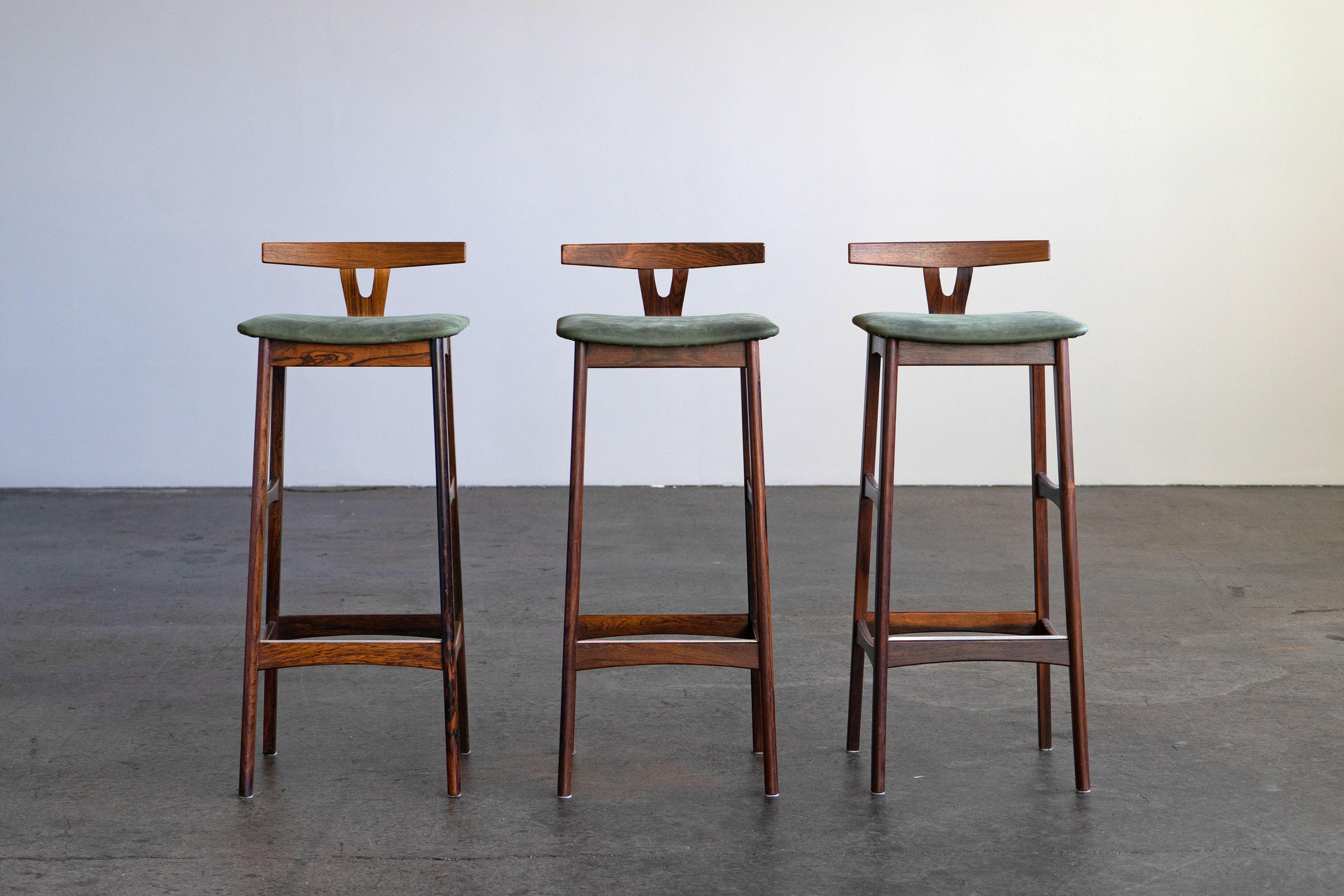 Set of three beautiful rosewood bar stools with green leather seats. The stools were designed by Knud Bent and produced by the Danish company Dyrlund in the 1960s. This set comes with a CITES-Certificate, which is transfered to the buyer.

Set