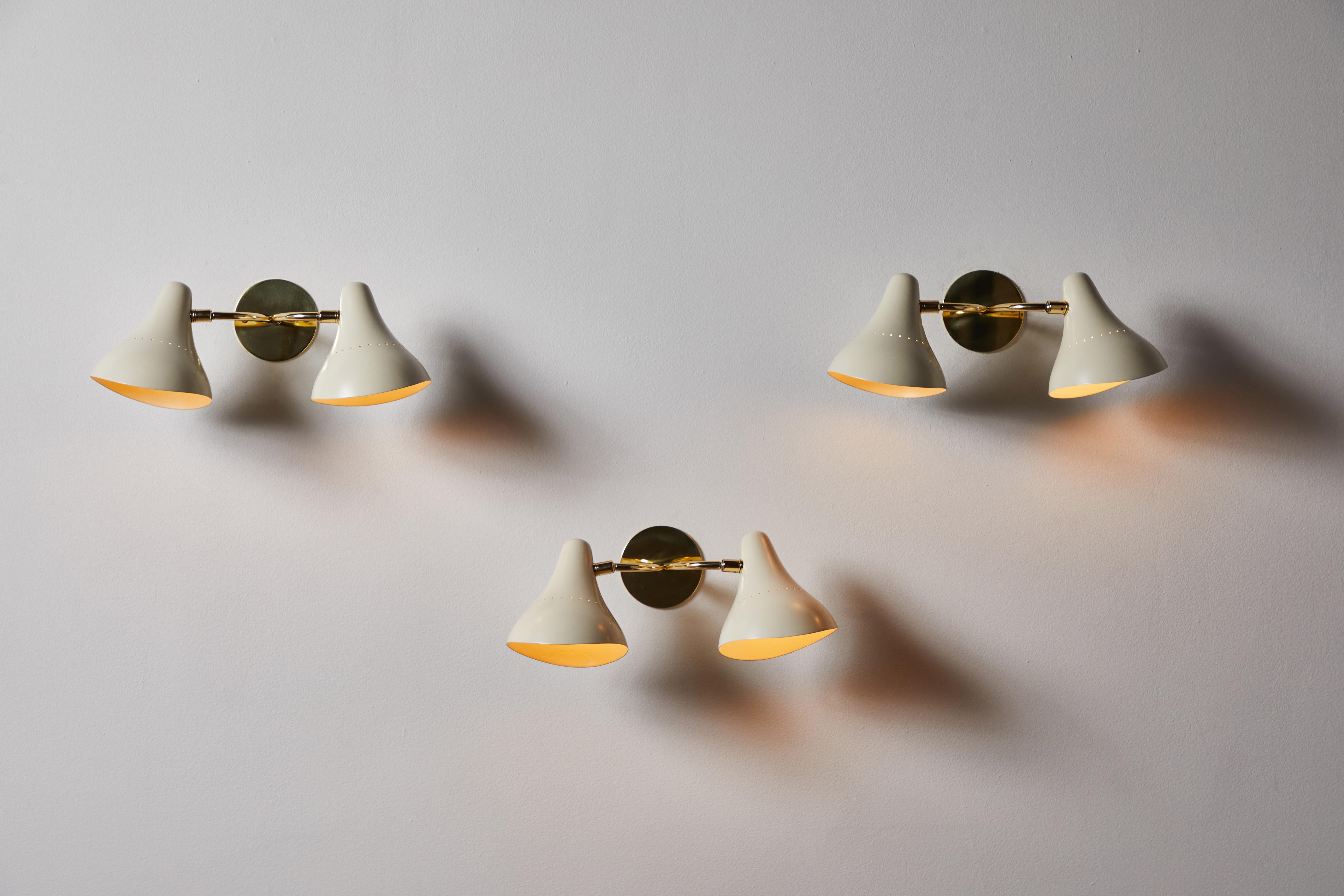 Two sconces by Giuseppi Ostuni for Oluce. Designed and manufactured in Italy, circa 1950s. Enameled metal, brass. Custom brass backplate. Shades articulate in various positions. Rewired for U.S. standards. We recommend one E27 100w maximum bulb per