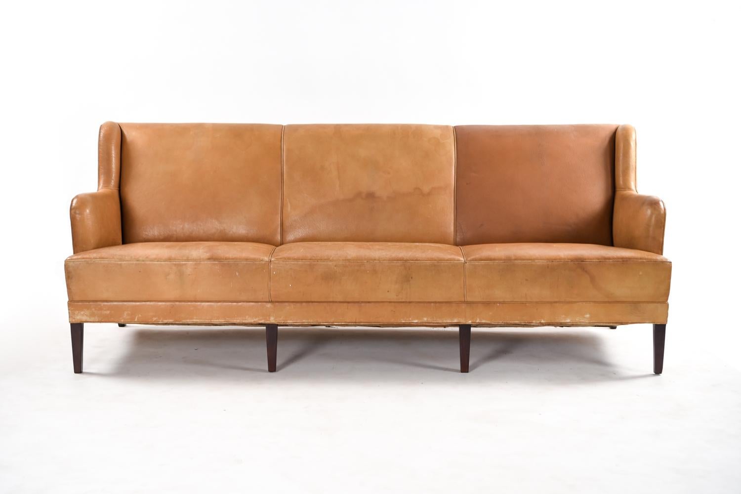 This three-seat sofa by Frits Henningsen has the original leather upholstery with incredible patination and mahogany legs. A wonderful example of early Danish modern design and production, with an art deco reminiscent shape of the body.