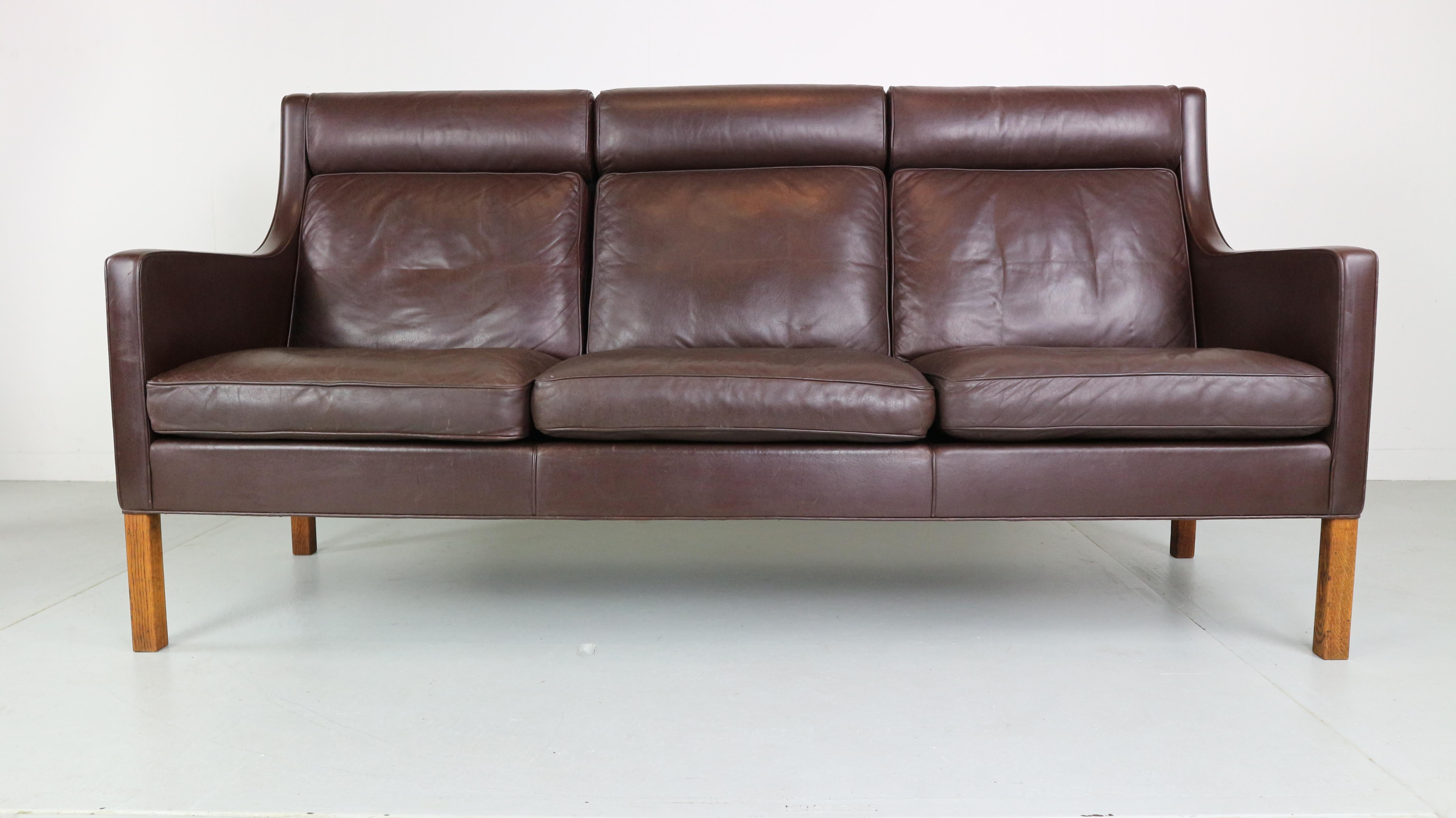 2433 model deep-brown three-seat leather sofa on the solid oak legs was designed by Børge Mogensen in the 1960s. This high back sofa was made in the 1970s by Fredericia Furniture in Denmark and is very comfortable, with the cushions remaining in a