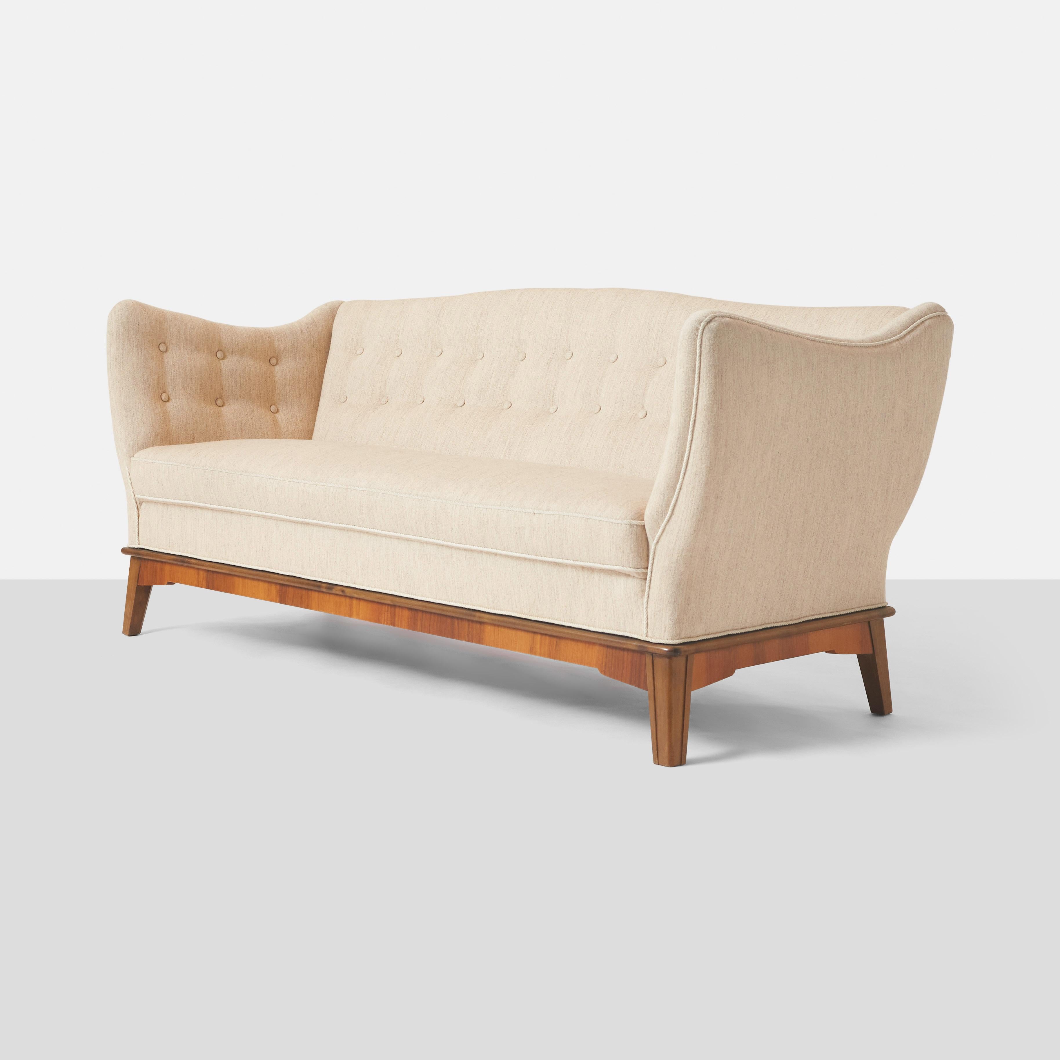 A three seat sofa designed by Stig Thoresen-Lassen and created by master cabinetmaker Louis G Thiersen. The base is made of mahogany and the body is covered in a beige wool. The sofa has a tight seat with tufting to the insides of the high arm rests