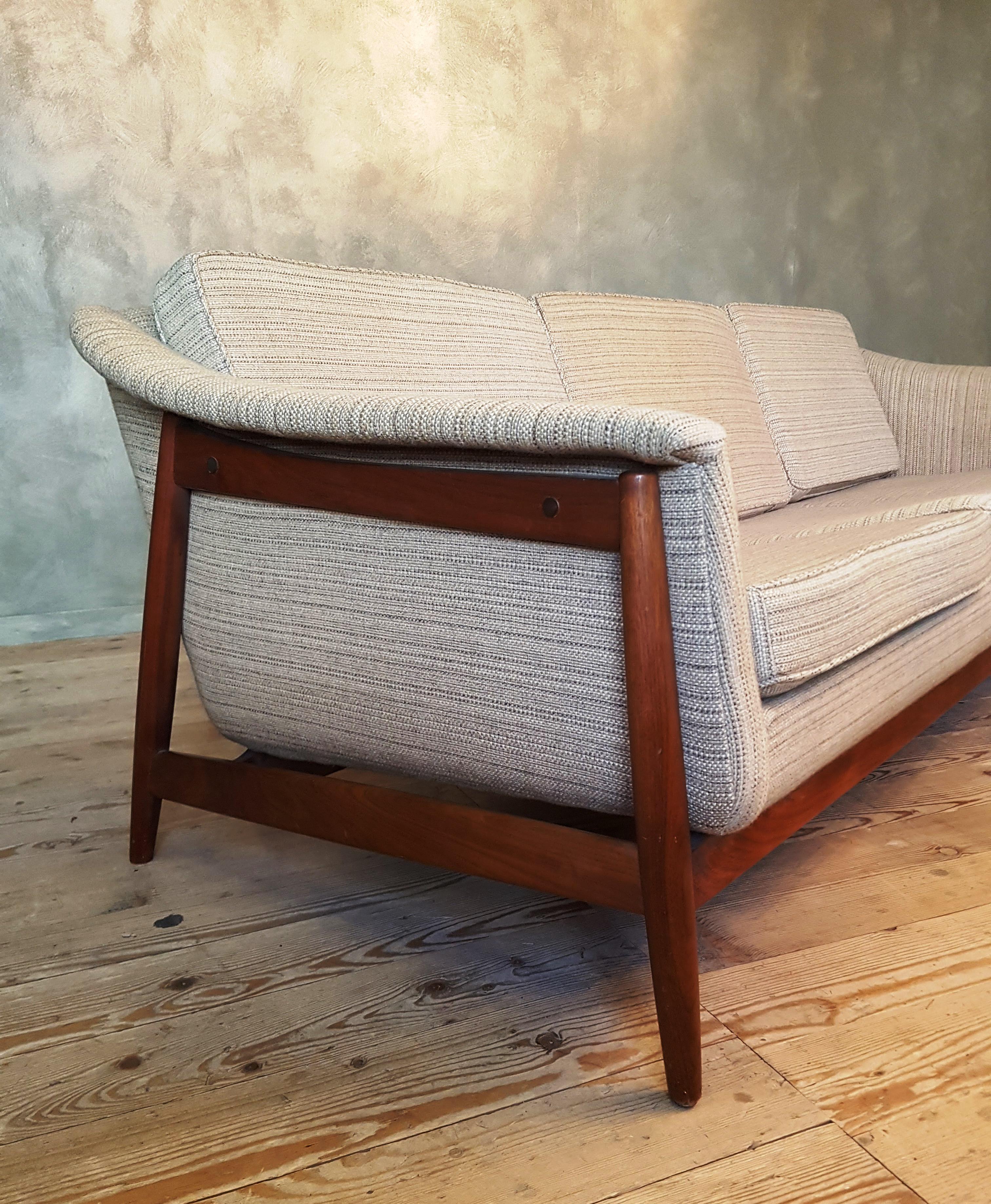 This 1950s three-seat sofa with curved armrests features a teak frame and a slatted back and has upholstered seating with webbing. It was designed around the 1950s and comes with a DUX label. The sofa is attributed to Folke Ohlsson and/or Alf