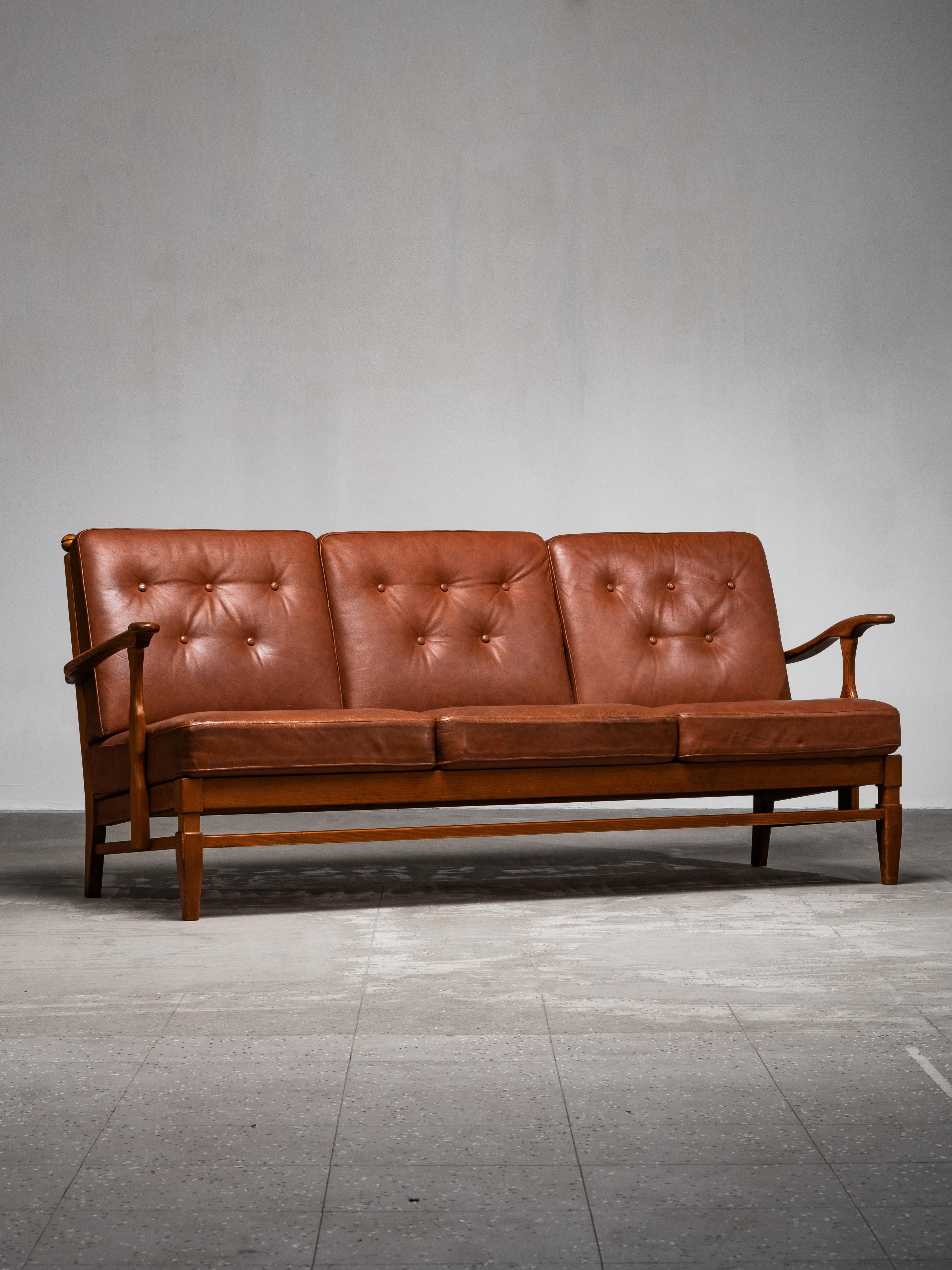 A fine example of early Swedish craftsmanship by Göperts Möbler, this three-seat sofa combines solid pine construction with original cognac-brown leather upholstery and spring cushions that provide both comfort and durability. The design reflects