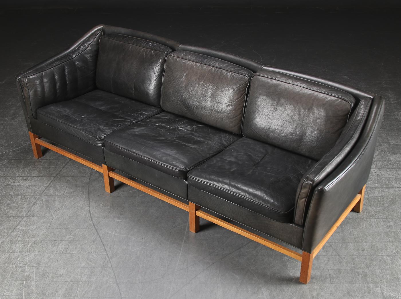 Comfortable three-seat sofa by Grandt furniture factory with solid oak frame, loose cushions in the back, seat and sides upholstered in leather. Danish Modern, 1970s. Measure: L 205 cm.