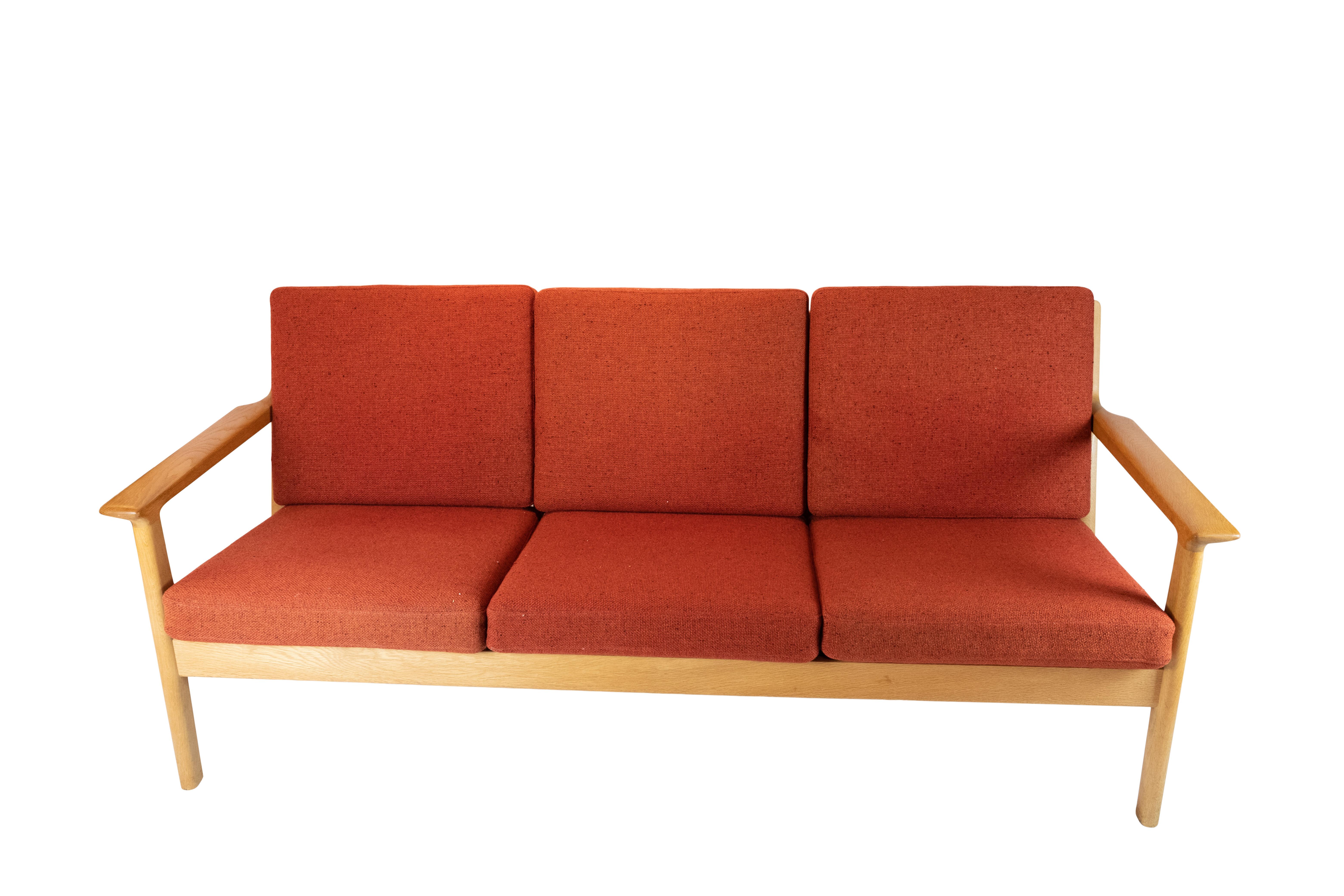 This three-seat sofa, a masterpiece of Danish design by the iconic Hans J. Wegner, epitomizes both elegance and comfort. Crafted from solid oak and upholstered in vibrant red wool fabric, it seamlessly blends timeless style with superior
