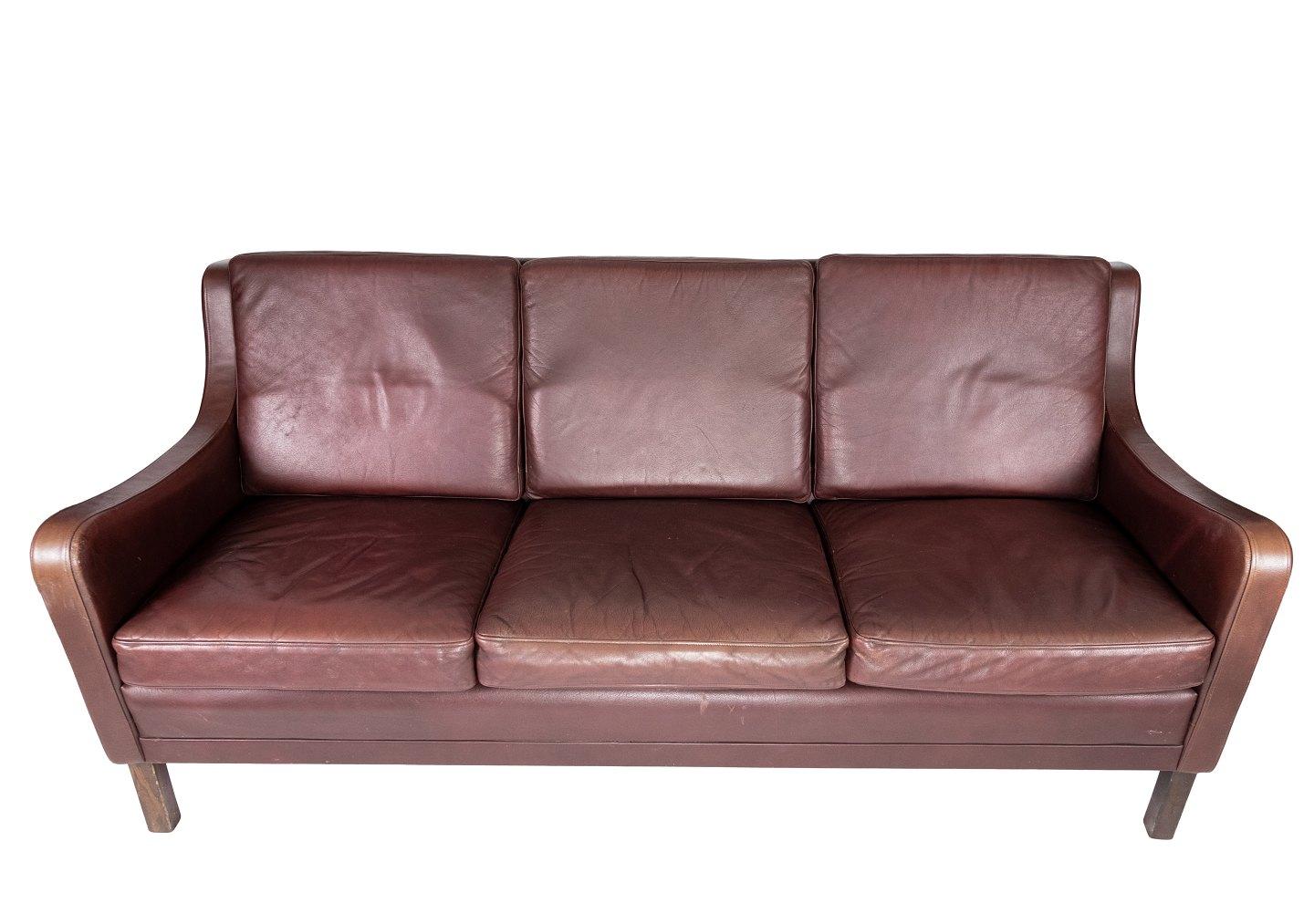 The three-seater sofa in red-brown leather from Stouby Møbler, produced in the 1960s, exudes timeless elegance and comfort. Stouby Møbler, a renowned Danish furniture company, is known for its high quality craftsmanship and timeless designs, and