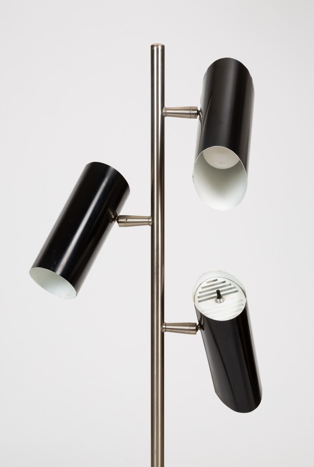A three shade floor lamp by Gerald Thurston for Lightolier. Distinguished by the unique, oblong canister shades, this lamp provides three-directional illumination from adjustable spots. The central column is polished steel, with enameled aluminum