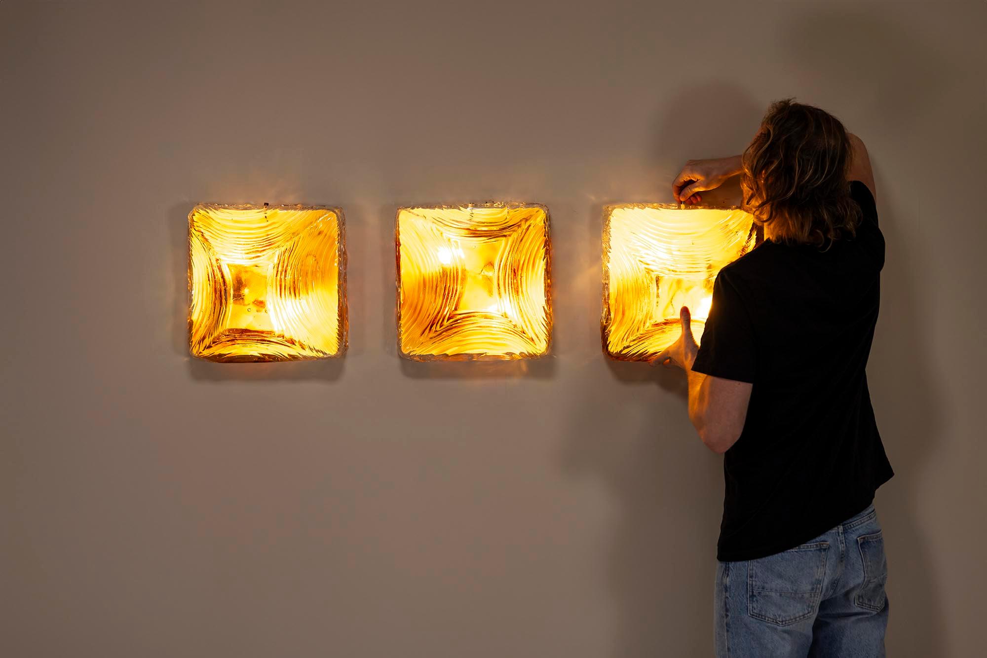 Imagine a trio of amber jewels elegantly adorning your wall, casting a warm, inviting glow. This stunning set of three wall sconces, crafted from Murano glass, embodies the unique charm of Italian hand-blown artistry. Even when the lights are off,