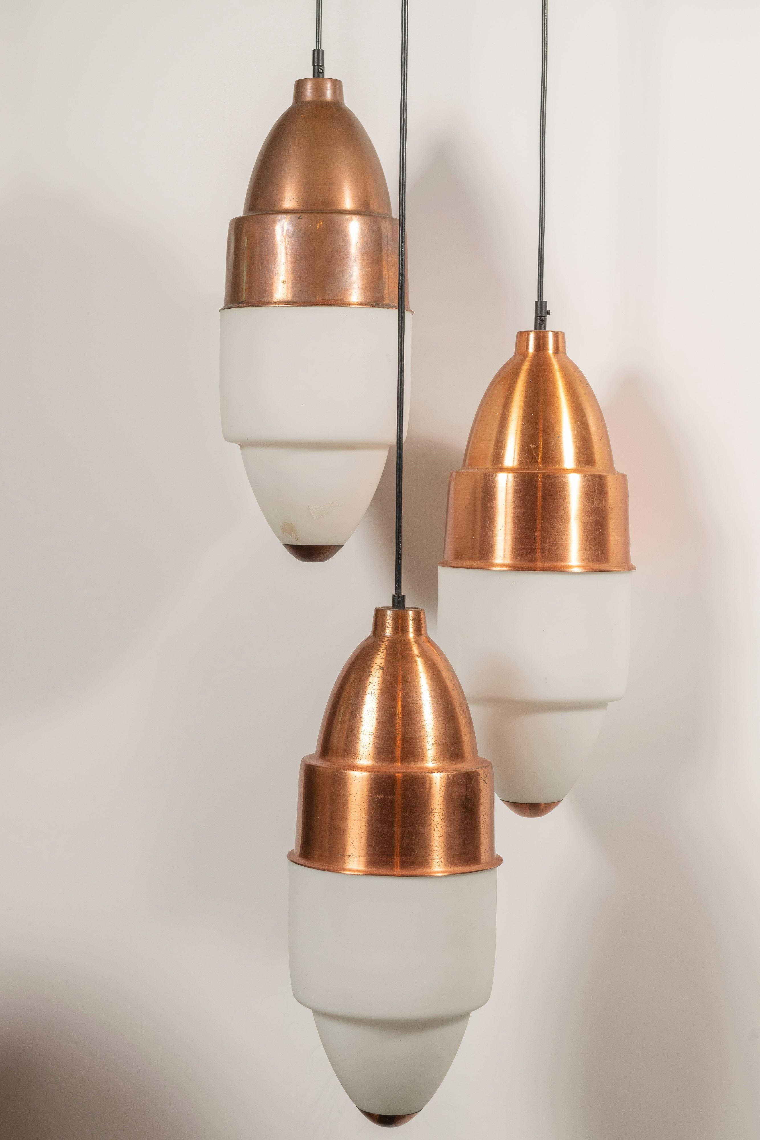 Three rare, mid-century copper and opaline glass pendants designed by Stilnovo, made in Italy. Presently wired with a plug, these lights can be hung in a cluster or individually and are perfect to create interest above a bar, kitchen island, dining