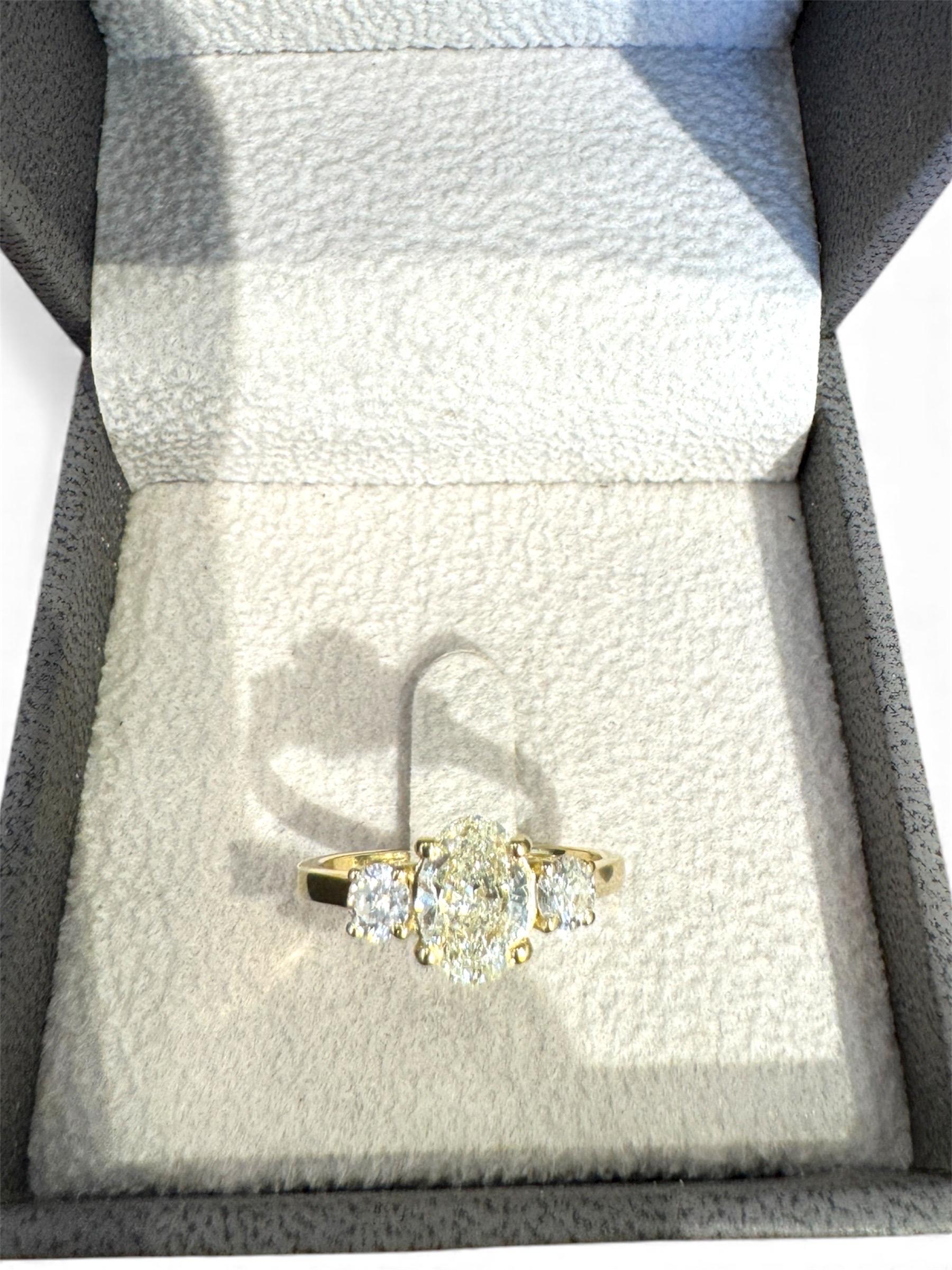 Une bague à trois pierres diamantées magnifiquement proportionnée, réalisée en or jaune 14 carats, présentant un mélange captivant d'élégance classique et de raffinement moderne. Au centre repose un diamant de taille ovale de 1,01 carat, admiré pour