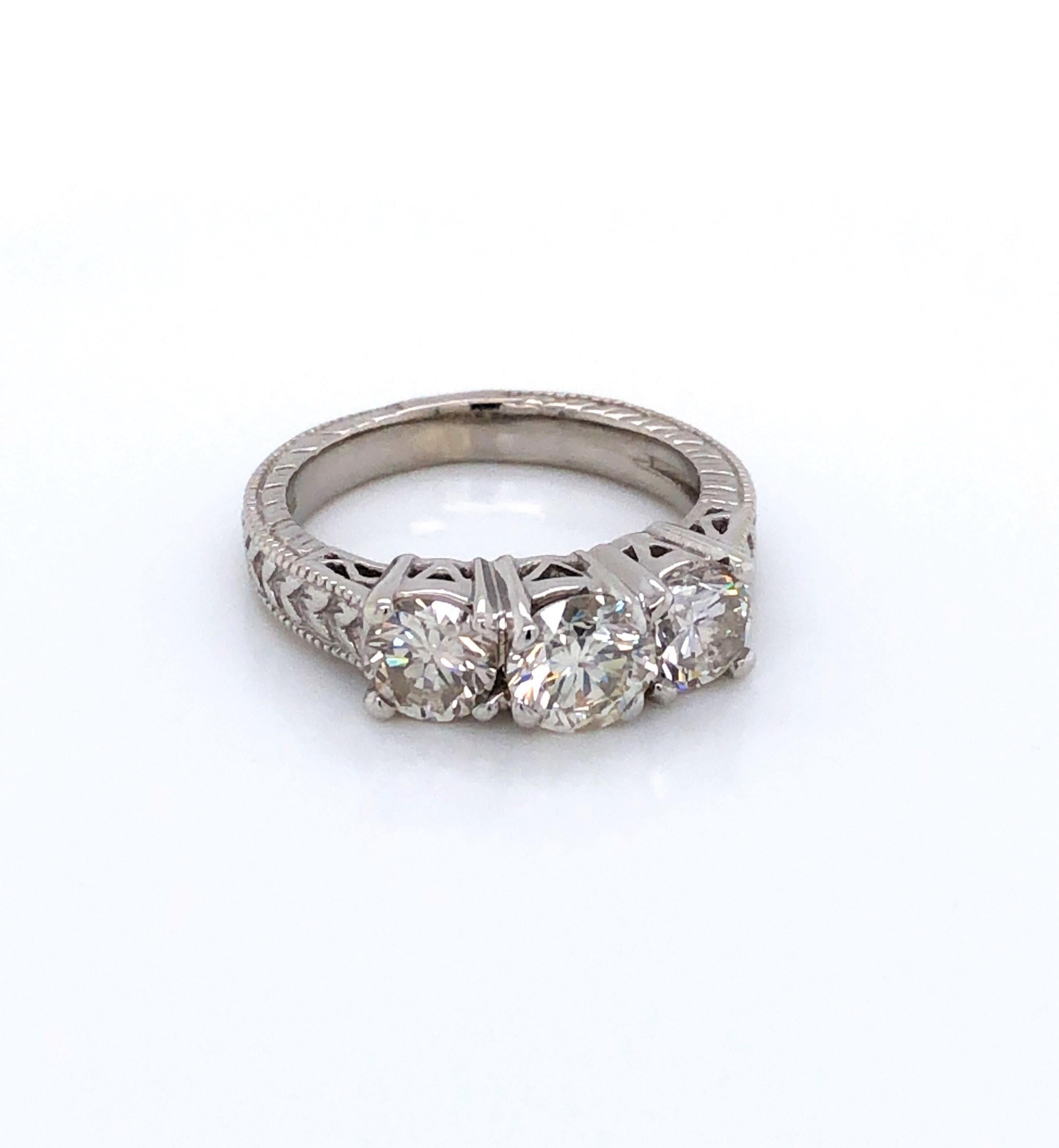 Admire the extra detail of the fancy fourteen karat 14k white gold antique style setting that adds to the classic beauty of this fine three stone diamond engagement ring. 
Prominently displayed are three round brilliant cut diamonds with the center