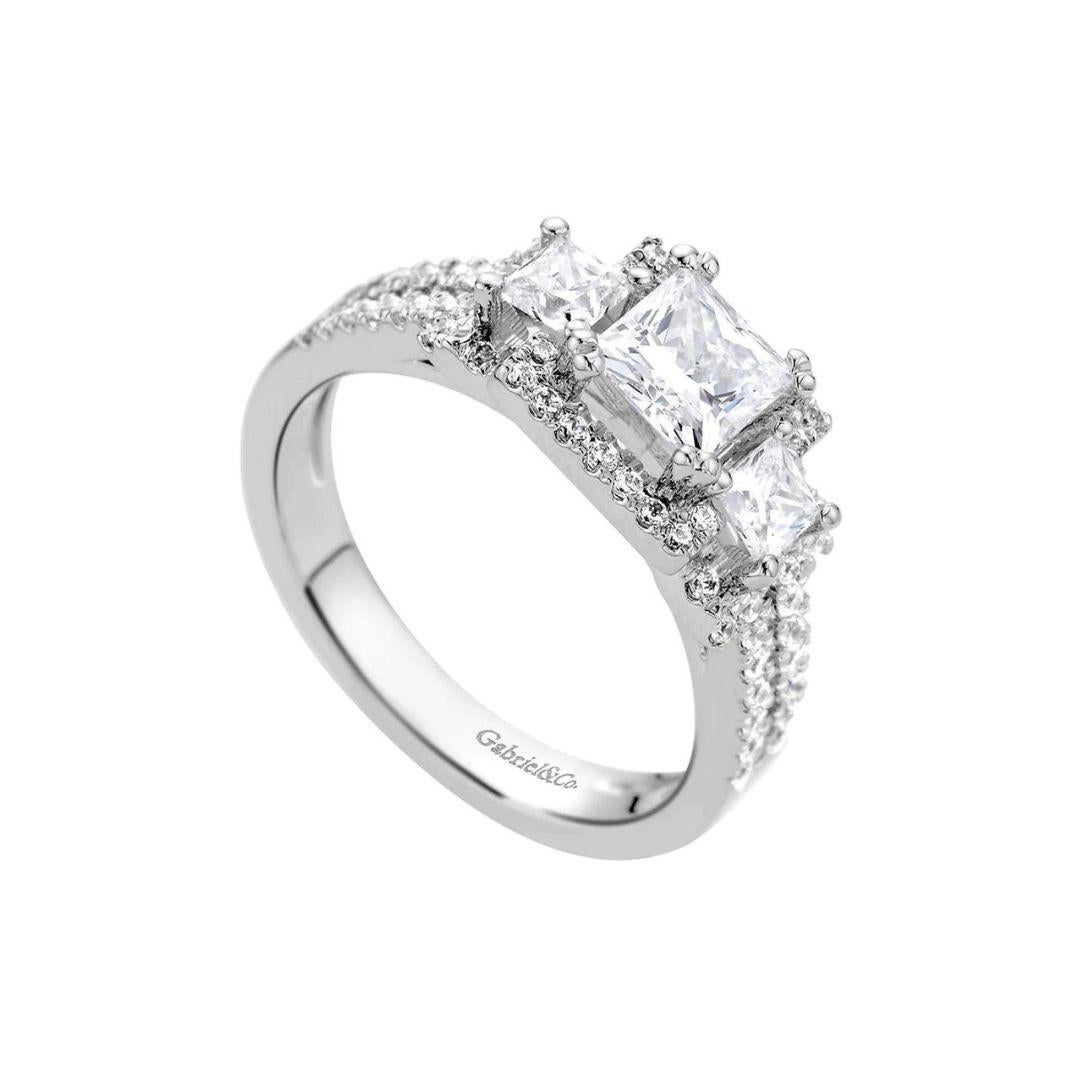 Non Traditional Three Diamonds Pave Set Engagement Mounting in 14k white gold. Double row, pave set diamond sides, lead up to two princess cut diamonds, flanking the center stone. Center diamond NOT included. Mounting head takes round brilliant cut,