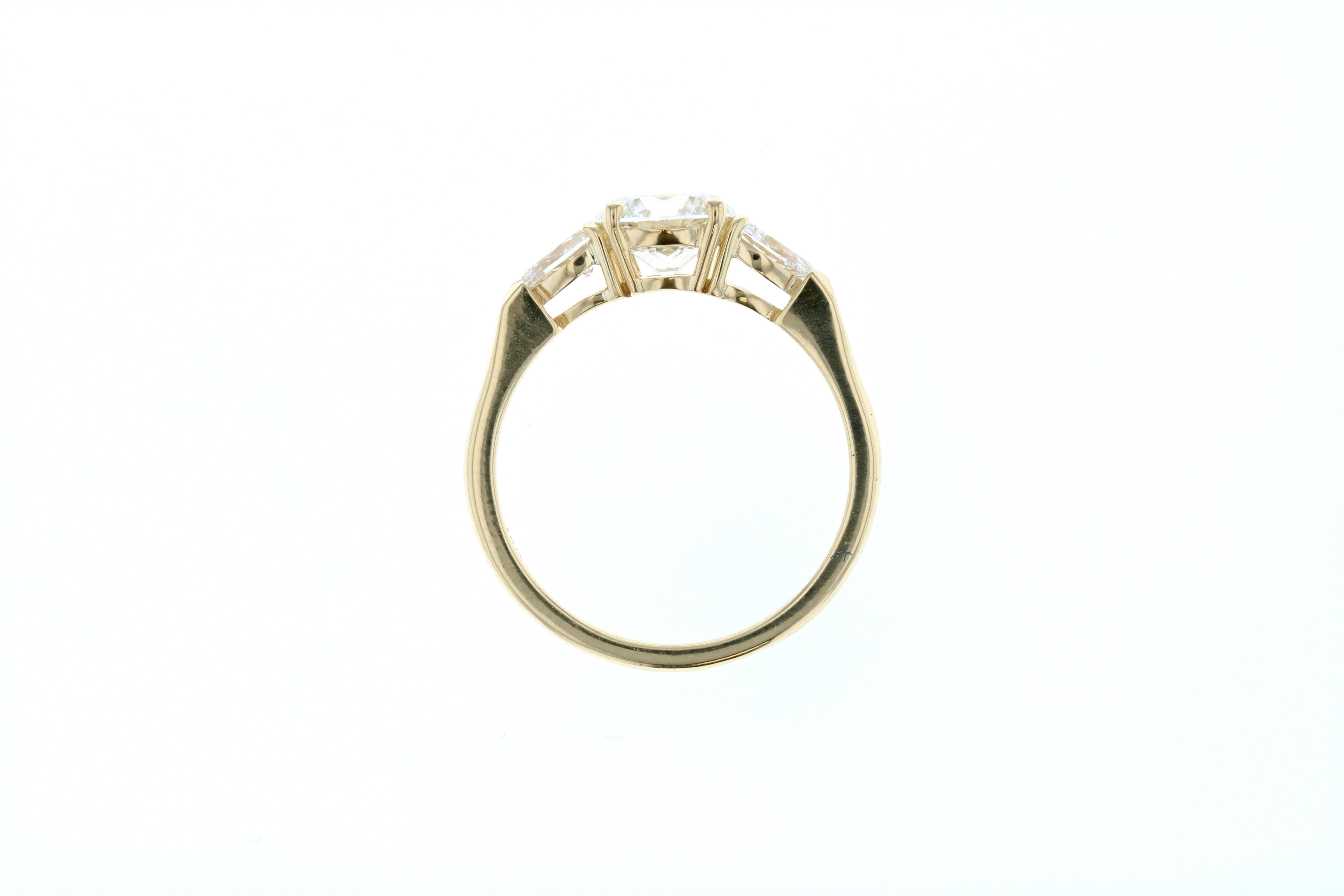 This stunning engagement ring is crafted in 18KT yellow gold, and contains a Round Diamond (1.13 total carat weight, H color, SI1 clarity) surrounded by 2 pear shape diamonds (0.39 total carat weight, H color, SI clarity). A perfect way to