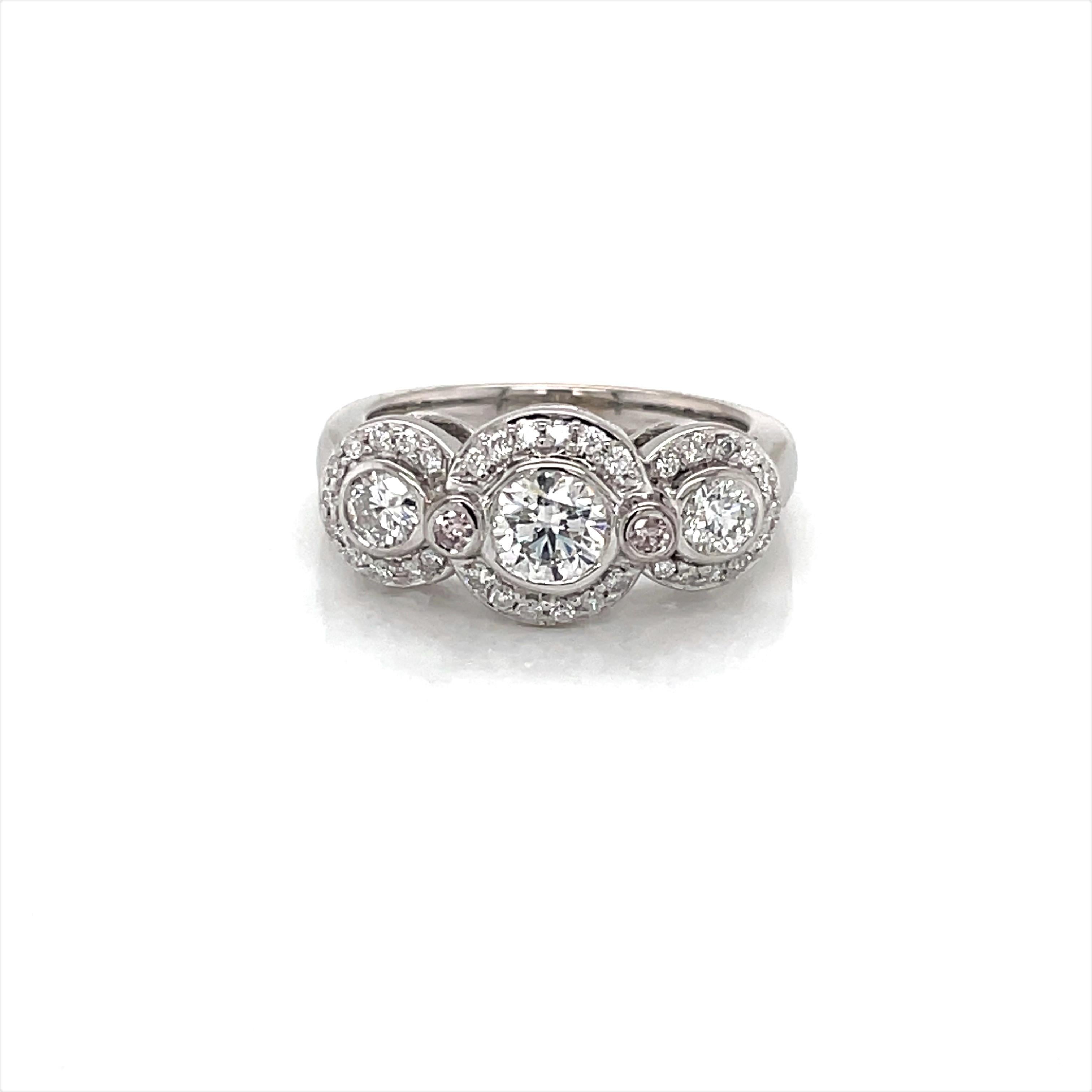 Over forty diamonds light up this brilliant three stone fourteen karat 14K white gold engagement ring. Sparking contoured diamond halos encircle the featured bezel set .60 carat center diamond and two .21 carat diamonds featured with accompanying