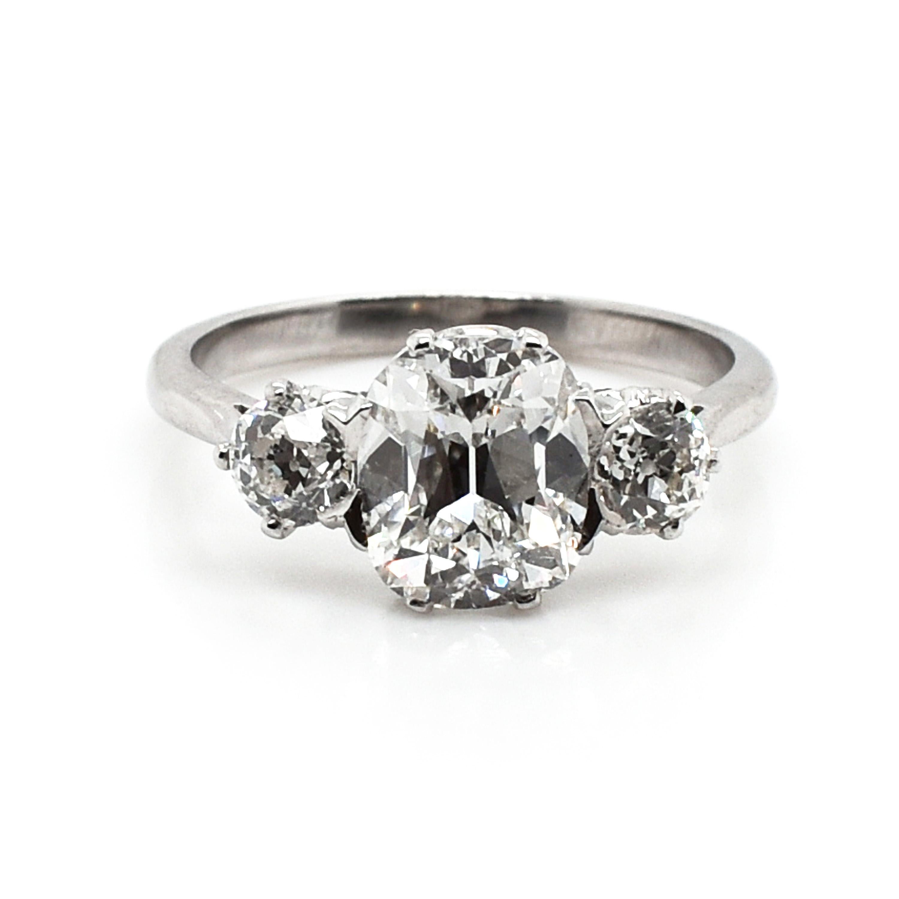 A three stone diamond ring set with a 2.01ct, E colour, VS1 clarity, cushion-cut diamond, with two old-cut diamonds set either side, with a total weight of 0.55ct, in claw settings, mounted in platinum, with tapered shoulders and a fine, pierced
