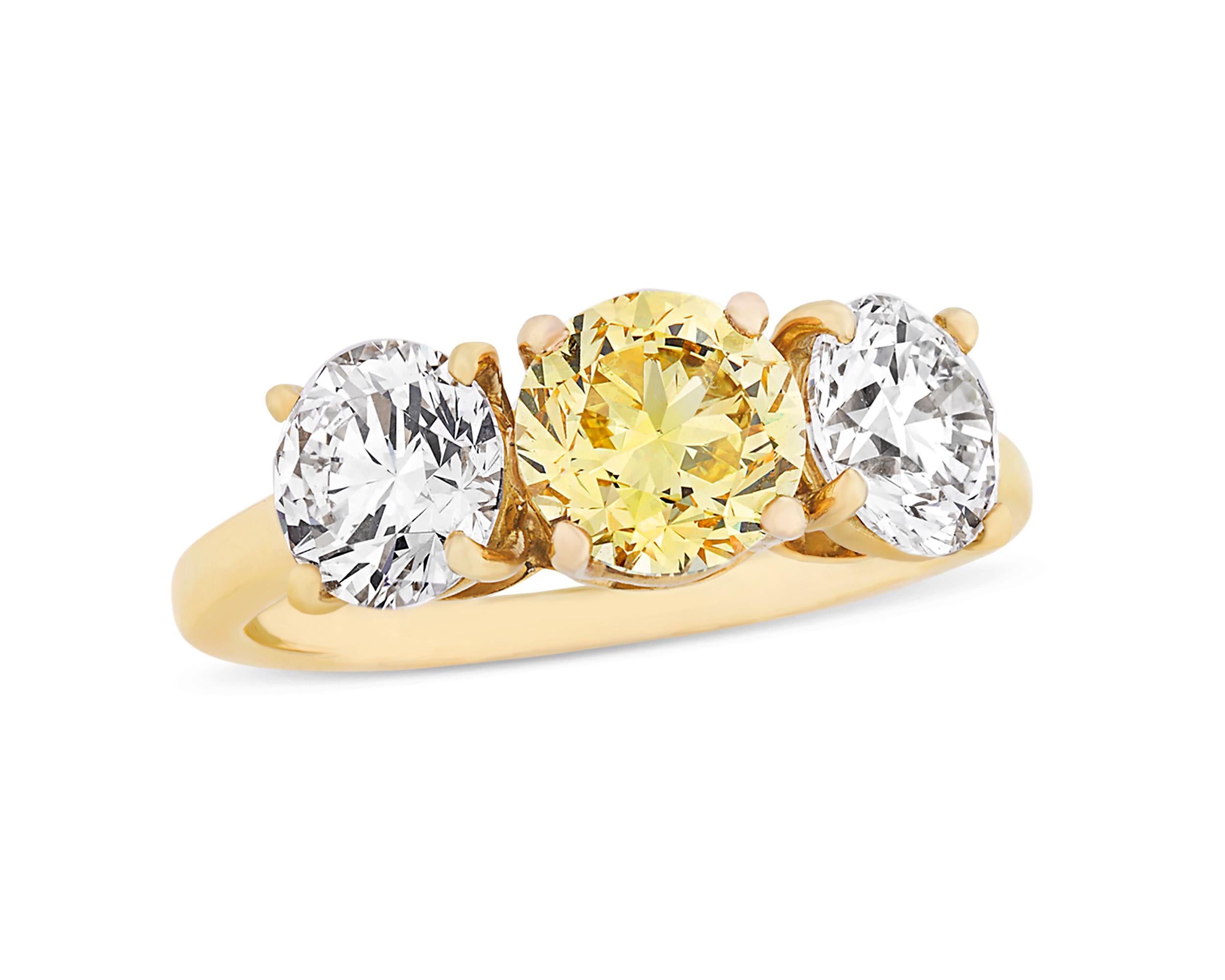 This classic three-stone ring from the celebrated house of Cartier is set with three extraordinary stones. At its center rests a round brilliant-cut fancy vivid yellow diamond weighing 1.24 carats. Certified by the Gemological Institute of America