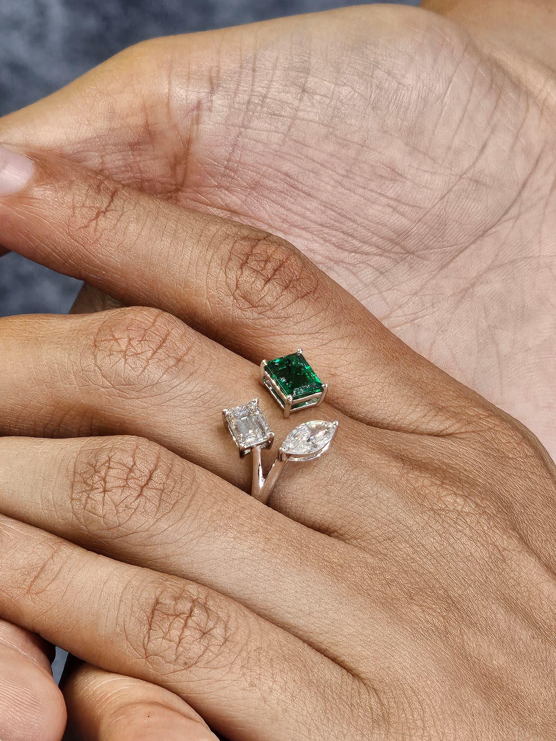 Espressione di eleganza senza tempo, questo anello in oro bianco 18 carati presenta un classico design a tre pietre con un vibrante smeraldo verde e due pietre a forma di fantasia.  diamanti. Lo smeraldo, noto per il suo colore ricco e per il suo