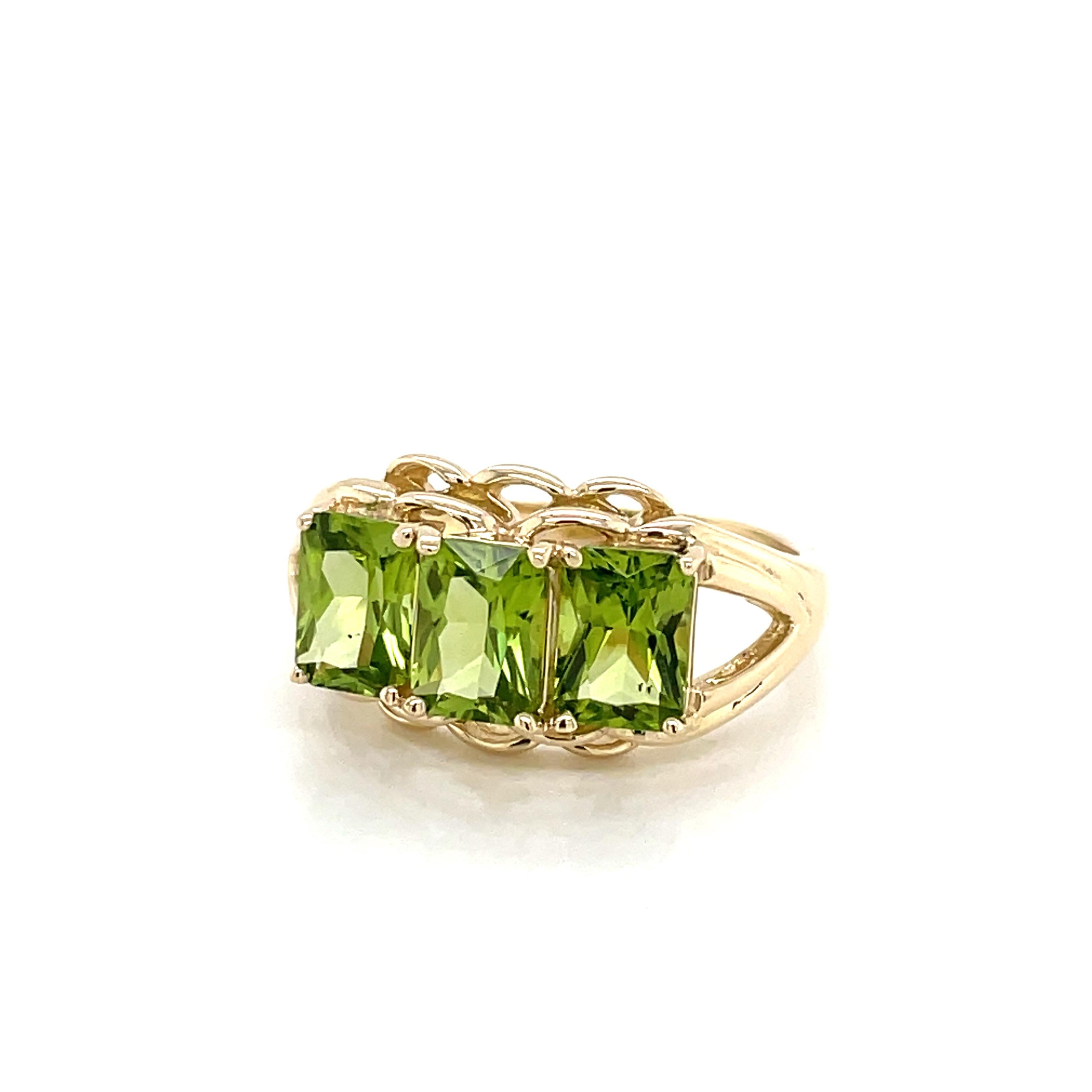 Alive and prominently displayed across the face of this gorgeous ring are three vibrant matching emerald cut peridot stones, each one carat, total weight 3 carats. In bright fourteen karat 14K yellow, a raised gallery of gold presents the striking