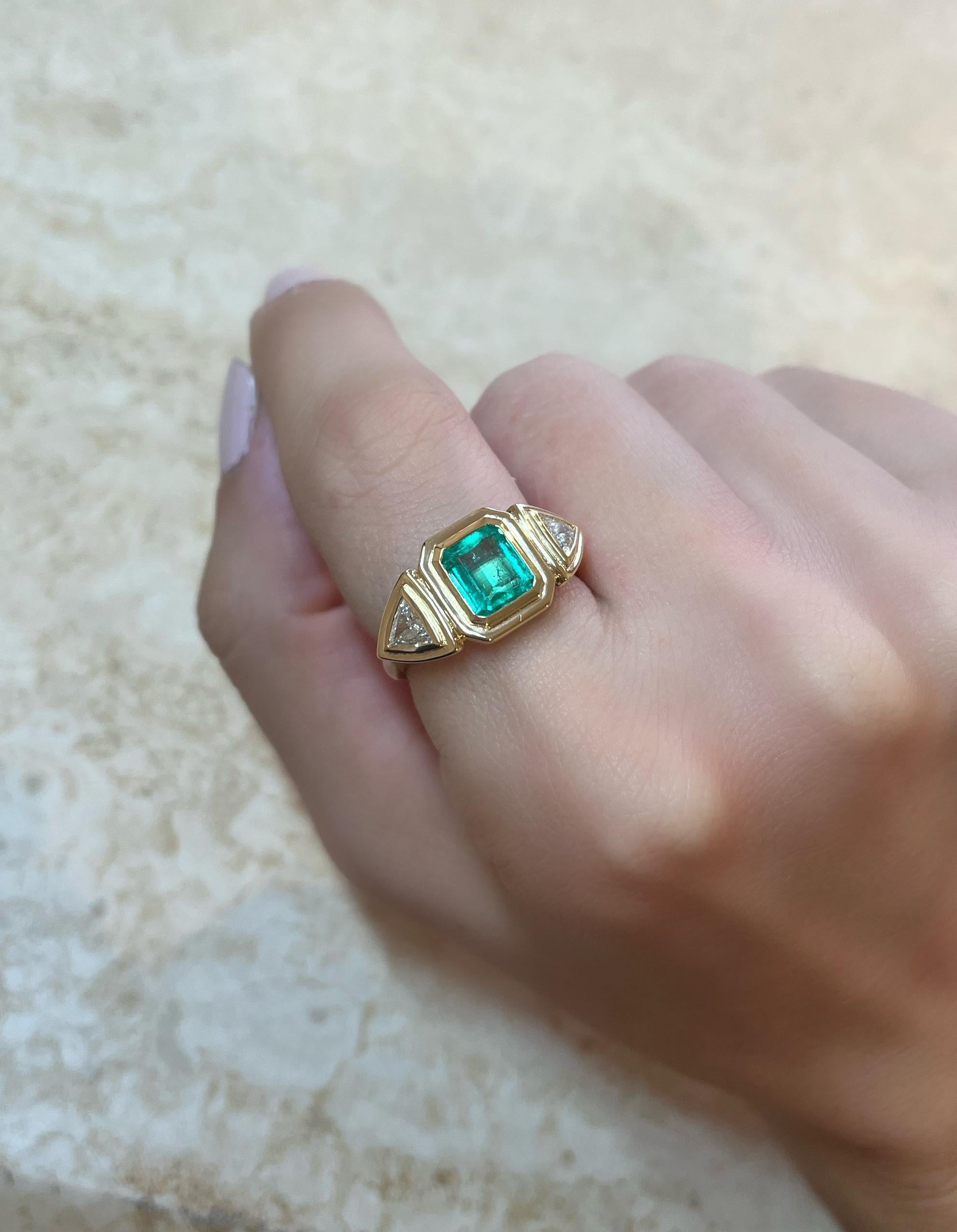 This exquisite 18-karat gold ring is centered with a natural emerald and paired with two natural trillion-cut diamonds, in a geometric stepped setting. 

The ring weighs just over 6 grams of gold, giving it a luxurious feel. It's three stone design