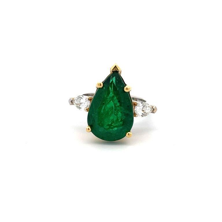 Take a moment to admire this breathtaking three-stone ring. The focal point is a stunning pear-shaped green emerald, considered the finest color for emeralds, weighing an impressive 6.79 carats. Accompanying the emerald are two marvelous pear-shaped