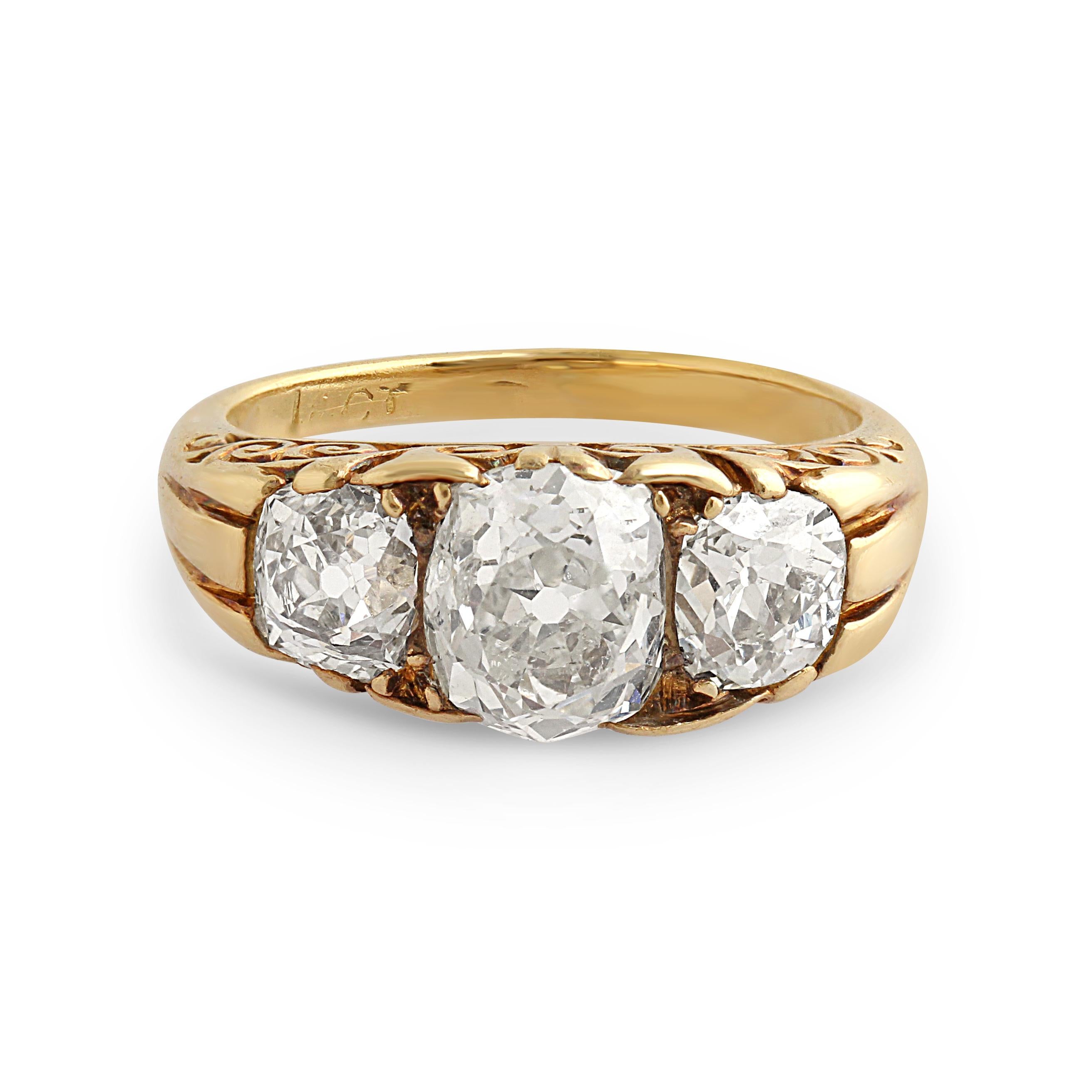 An antique three stone diamond ring set with three old cushion-cut diamonds in an 18k yellow gold mount with scrolling details. Circa 1890s. Size = M. Weight = 6.40gr.