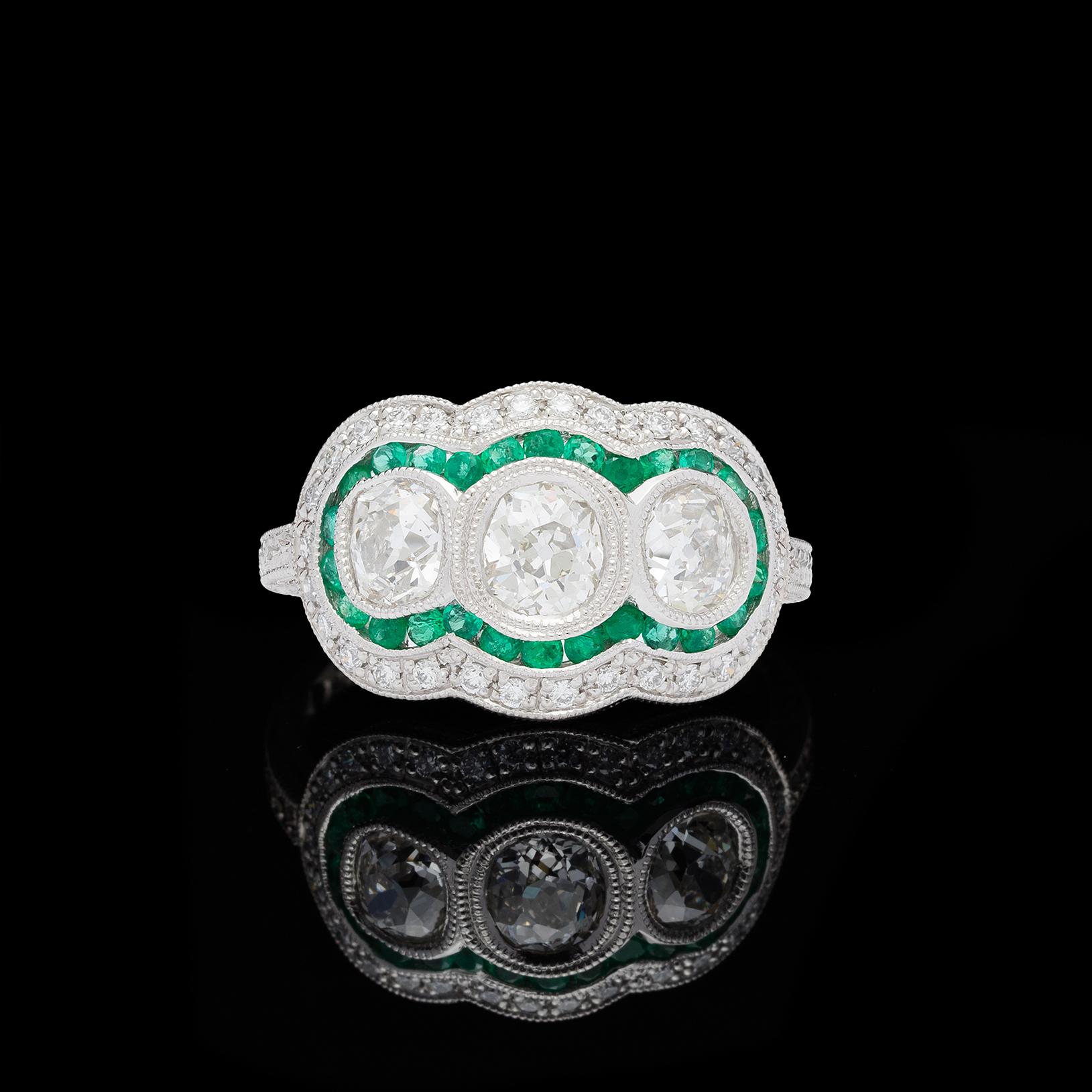 Tre diamanti antichi di vecchio taglio europeo riutilizzati per un totale di 1,32 carati (H-I e VS-SI) incastonati in un'intricata montatura in platino in stile edoardiano. Un'aureola di smeraldi taglio rotondo del peso di 0,36 carati in un vibrante