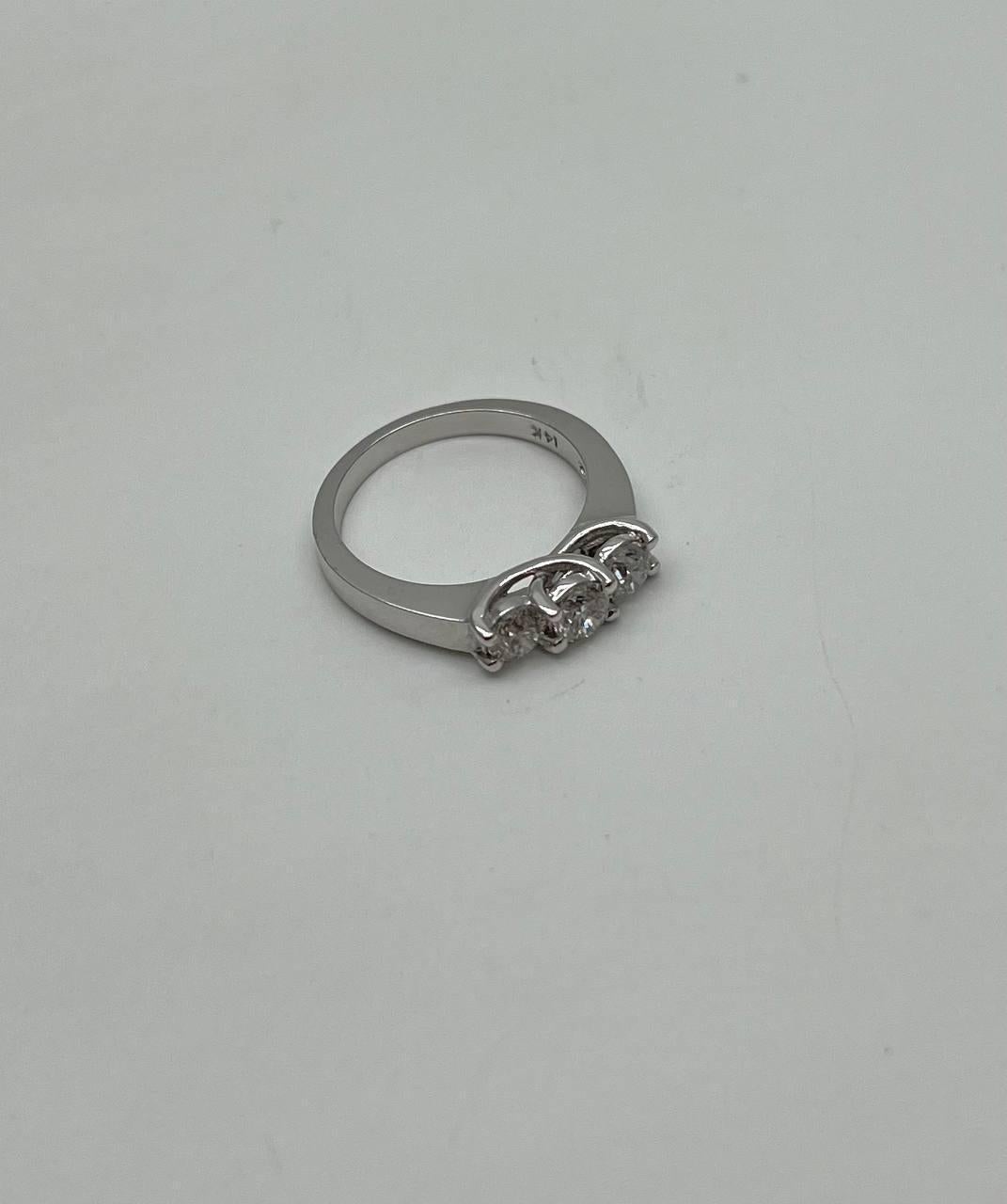 Dieses exquisite Stück besticht durch sein elegantes Design aus poliertem 14-karätigem Weißgold. Der Ring zeigt drei Diamanten im Rundschliff, die jeweils in einer sicheren Zackenfassung gefasst sind. Die Steine sind in einer linearen Formation