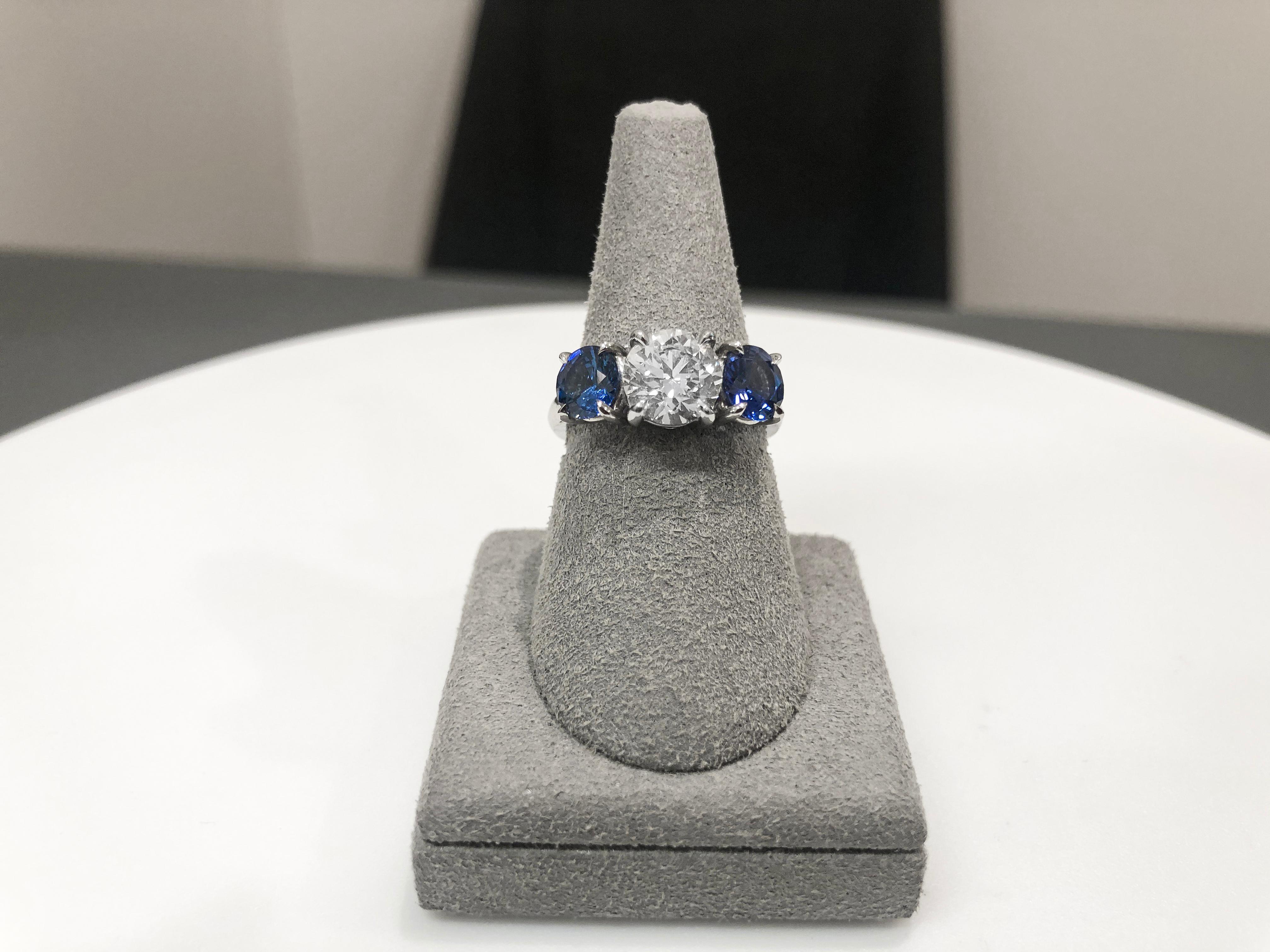 A sparkling 1.50 carat round diamond takes center stage in this sapphire and diamond engagement ring. Accenting the center stone are 2 color-rich rubies set in 4 prongs made in platinum. Rounded composition for a seamless and comfortable fit. Size 6