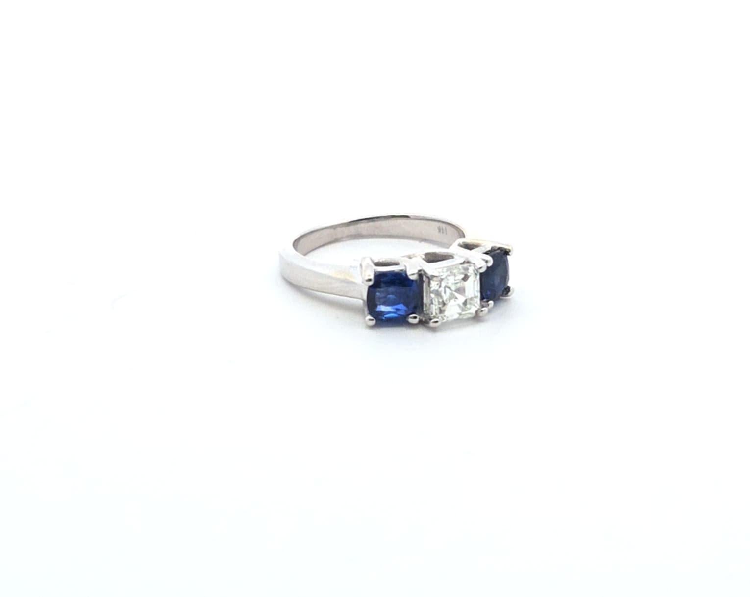 Als zeitloses Symbol der Eleganz zeigt dieser Dreisteinring einen Brillanten im Prinzessinnenschliff in der Mitte, flankiert von zwei tiefblauen Saphiren. Der auffällige Kontrast zwischen dem funkelnden Diamanten und den reichen Saphiren an den