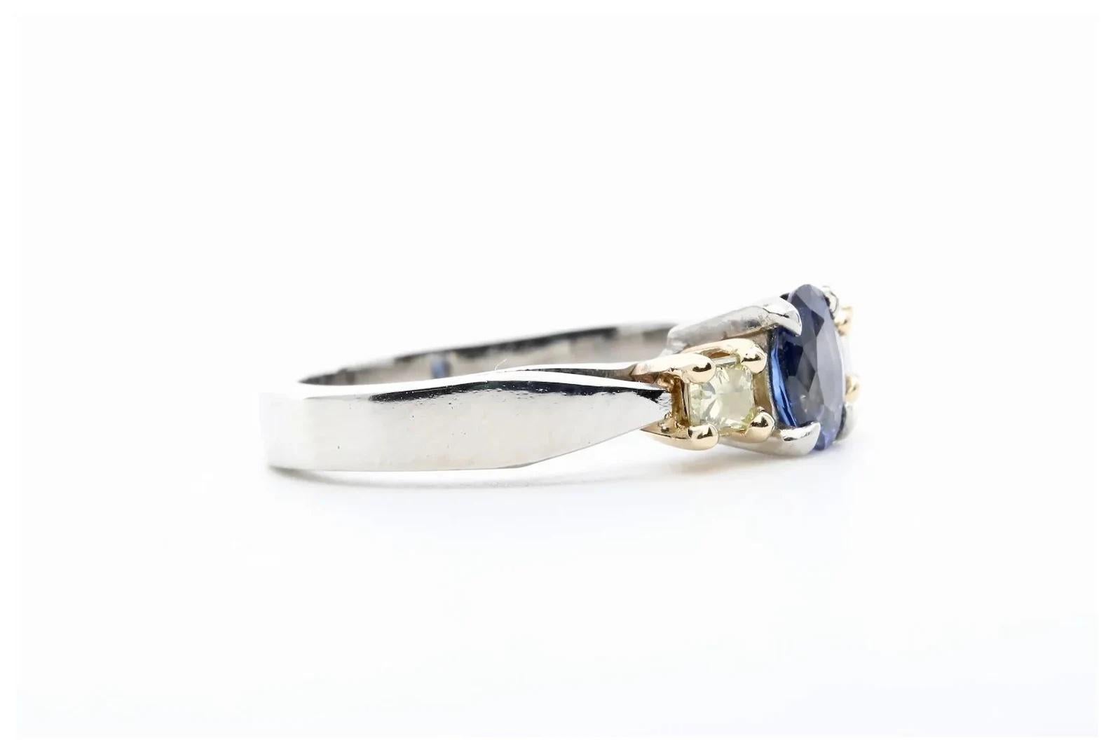 A three stone sapphire, and diamond ring in platinum and 18 karat yellow gold. Centering this ring is a 0.70 carat natural, no heat oval sapphire of beautiful vivid blue color. Framing the sapphire are a pair of 0.30ctw princess cut fancy yellow