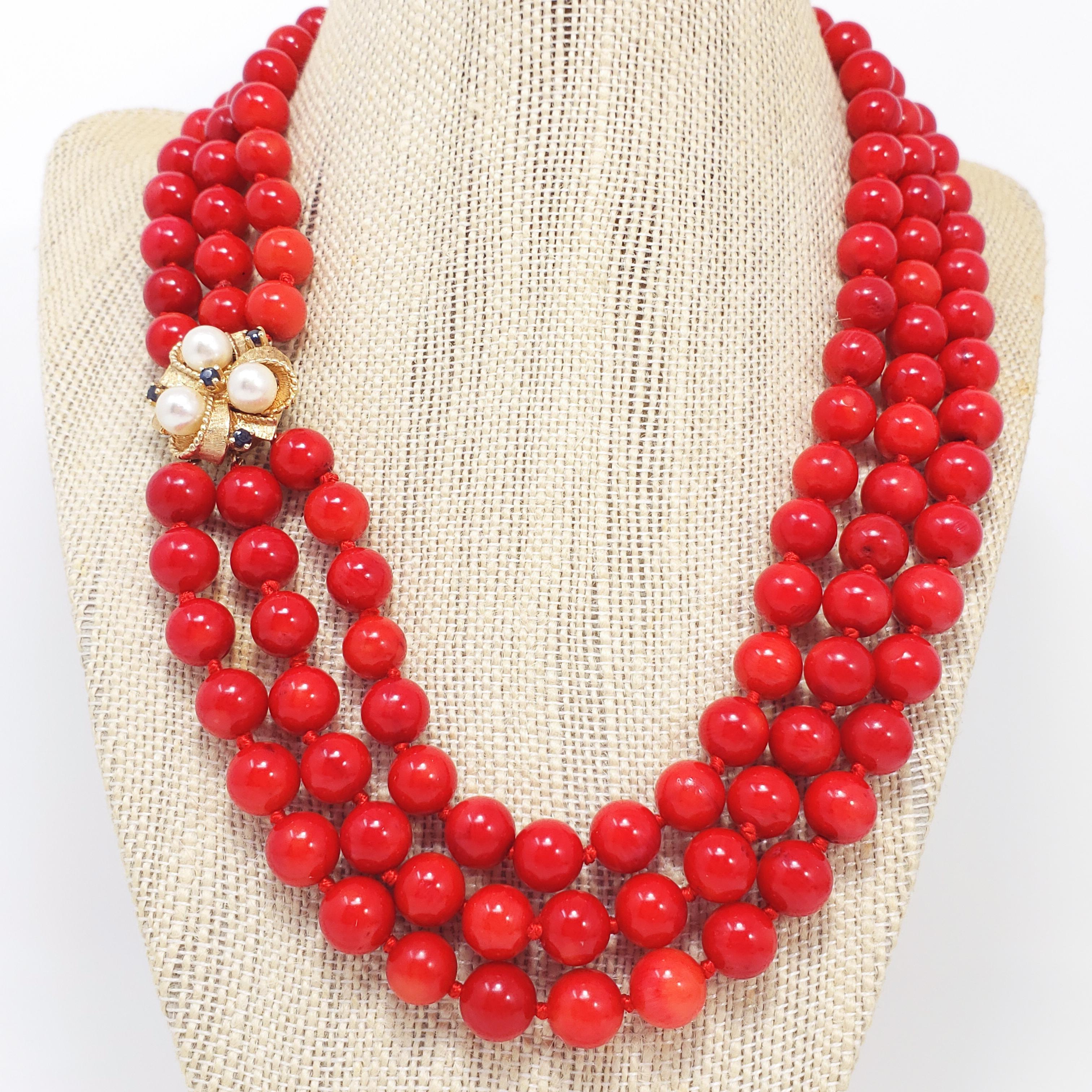An exquisite necklace featuring three strands of 9mm genuine red,  Italian coral beads on a regal 14K gold box clap. The clasp features a bow motif and is decorated with three 6.5mm genuine pearls and four 2.3mm genuine, prong-set sapphires. A