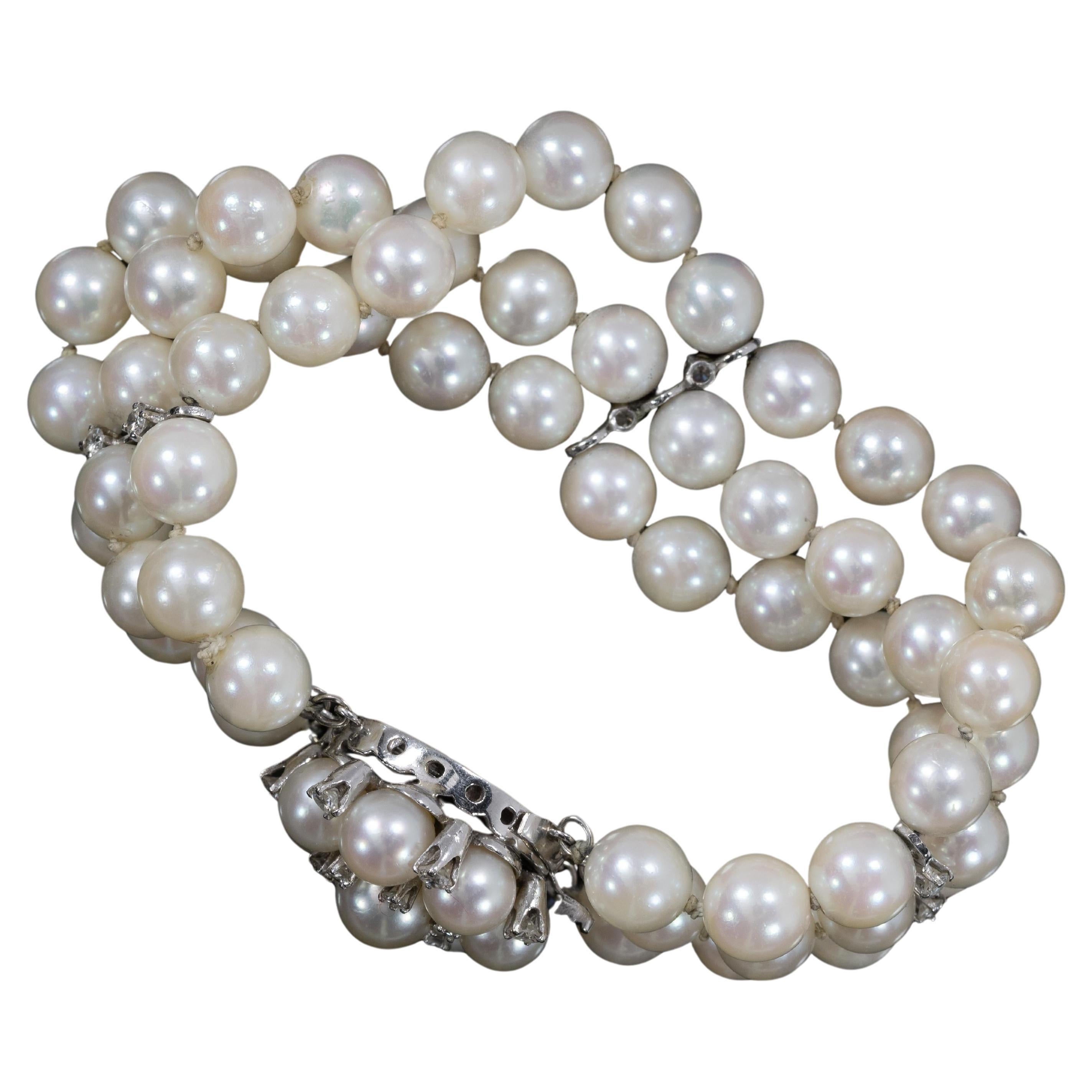 Dieses elegante Armband besteht aus drei schimmernden Perlensträngen, die mit schillernden Diamanten besetzt sind, alle in 14-karätigem Weißgold. Die Stränge werden durch eine dekorative Blumenschließe ergänzt, die mit komplizierten Diamantdetails