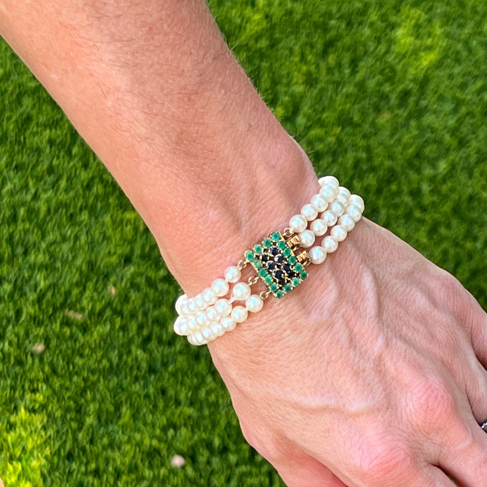 Mid twentieth century multi-strand pearl bracelet with a beautiful sapphire and emerald clasp. The three strands of cultured white pearls feature a rectangular 14 karat yellow gold clasp set with round cut blue sapphires and emeralds. The clasp