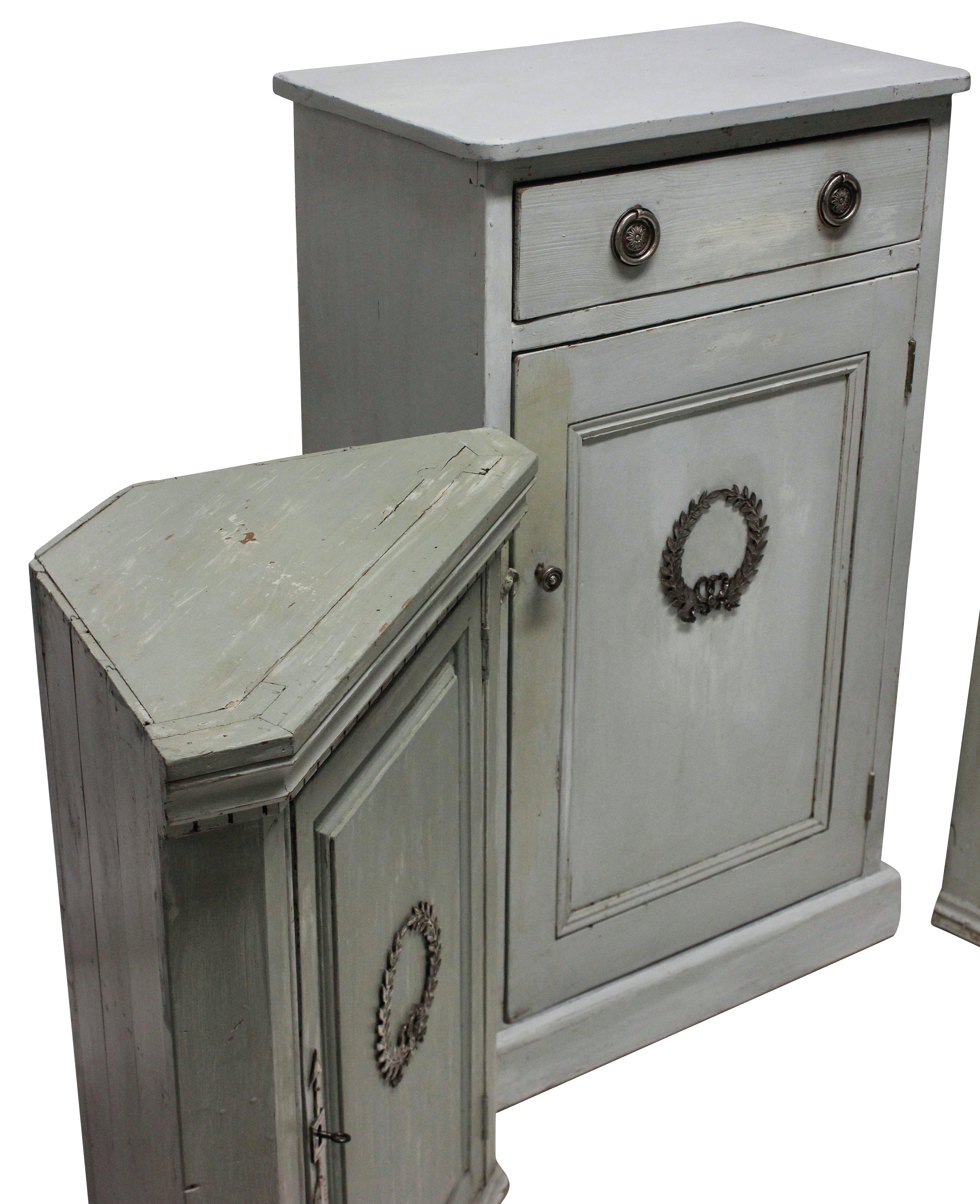 A set of three painted Swedish cupboards, comprising a larger cupboard with drawer and two floor standing corner cupboards, each with a shelf. The exteriors decorated with silver plated bronze mounts.

Measures: Large cupboard 106 high x 38 deep x