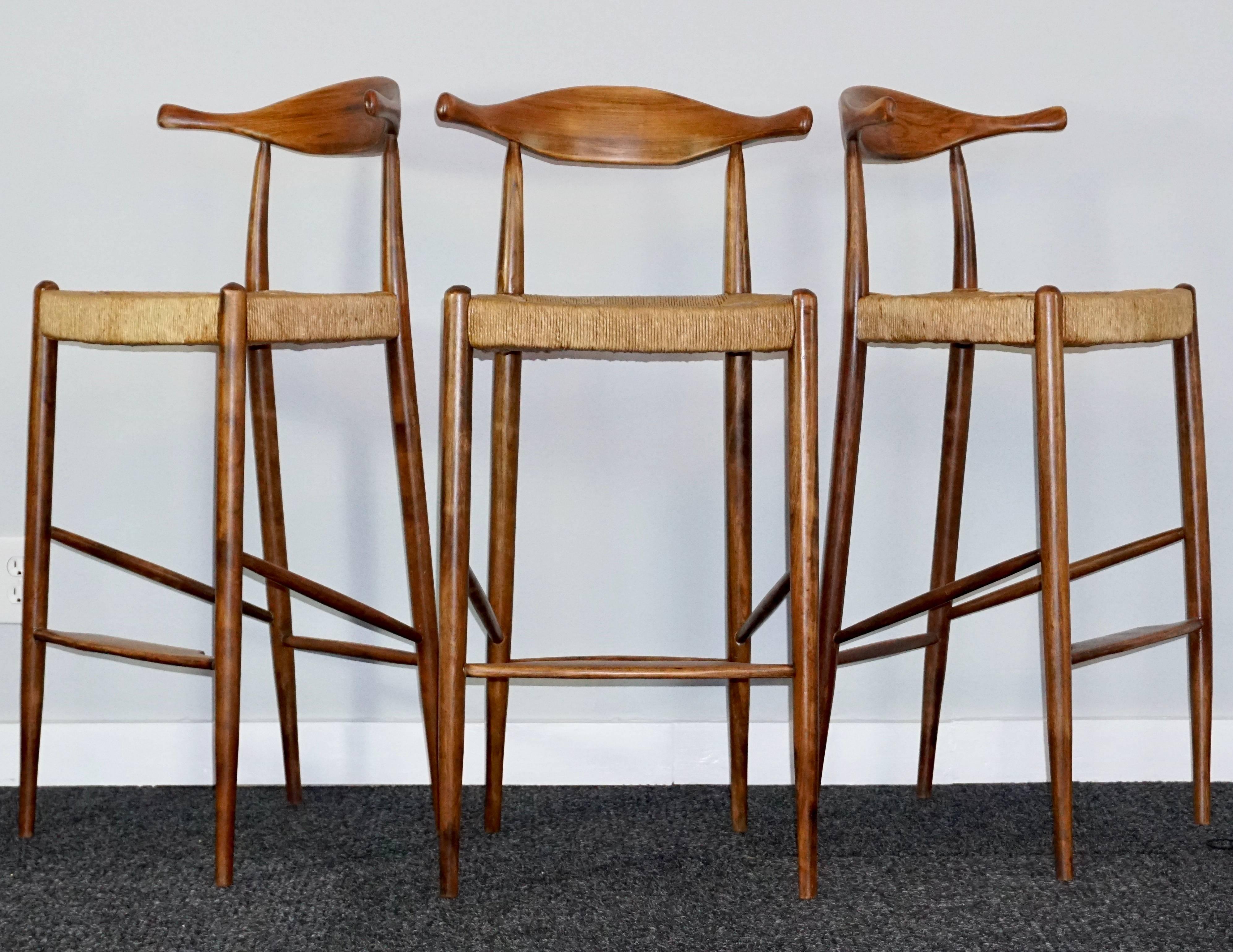 Arthur Umanoff
Set of three (3) teak and rush rattan seated cow horn stools designed and manufactured in the early 1960s.

Measure: Height 39 inches 
Width 18 inches
Depth 15 inches

