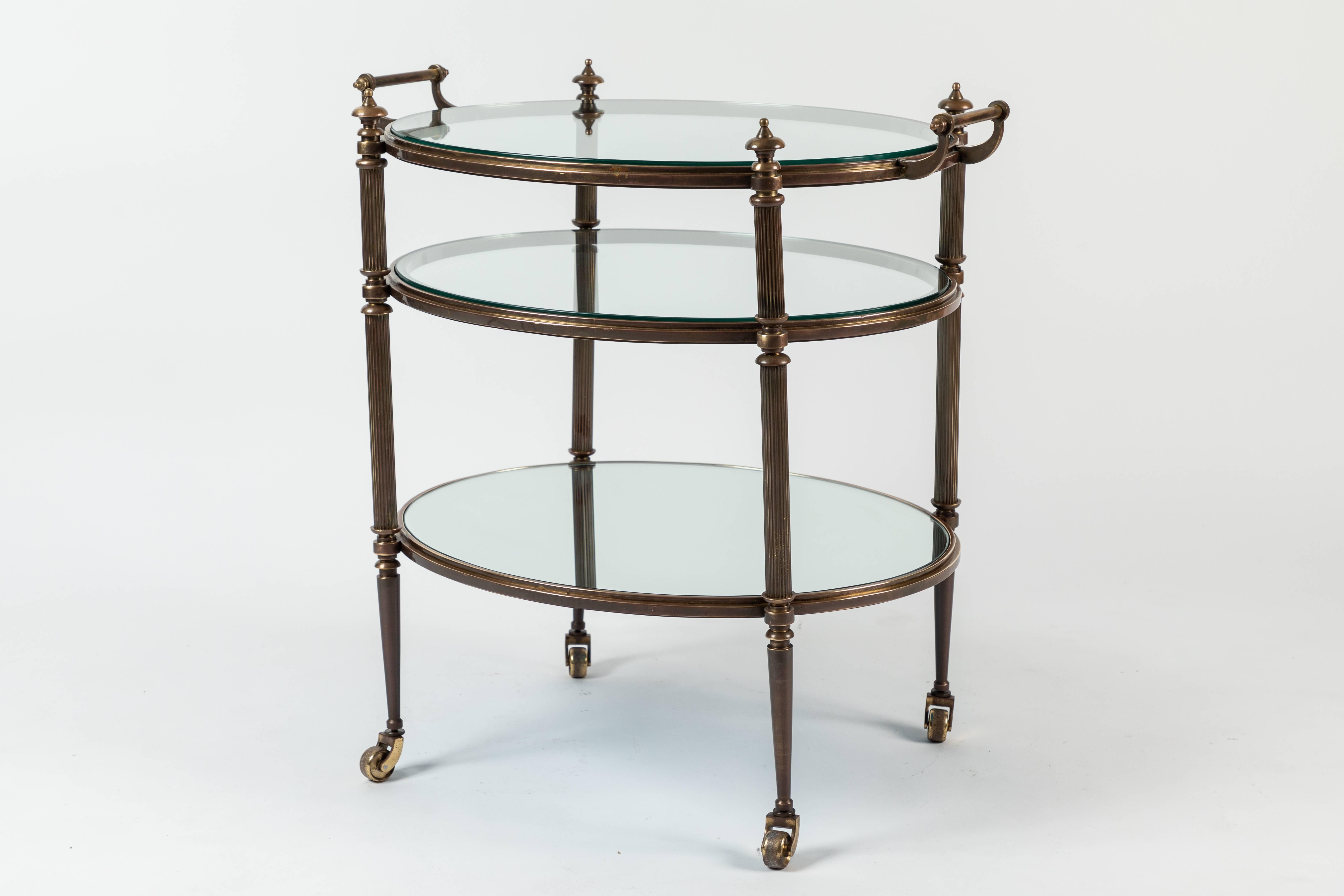 A beautifully patinated three-tier brass and glass drinks trolley on brass castors.