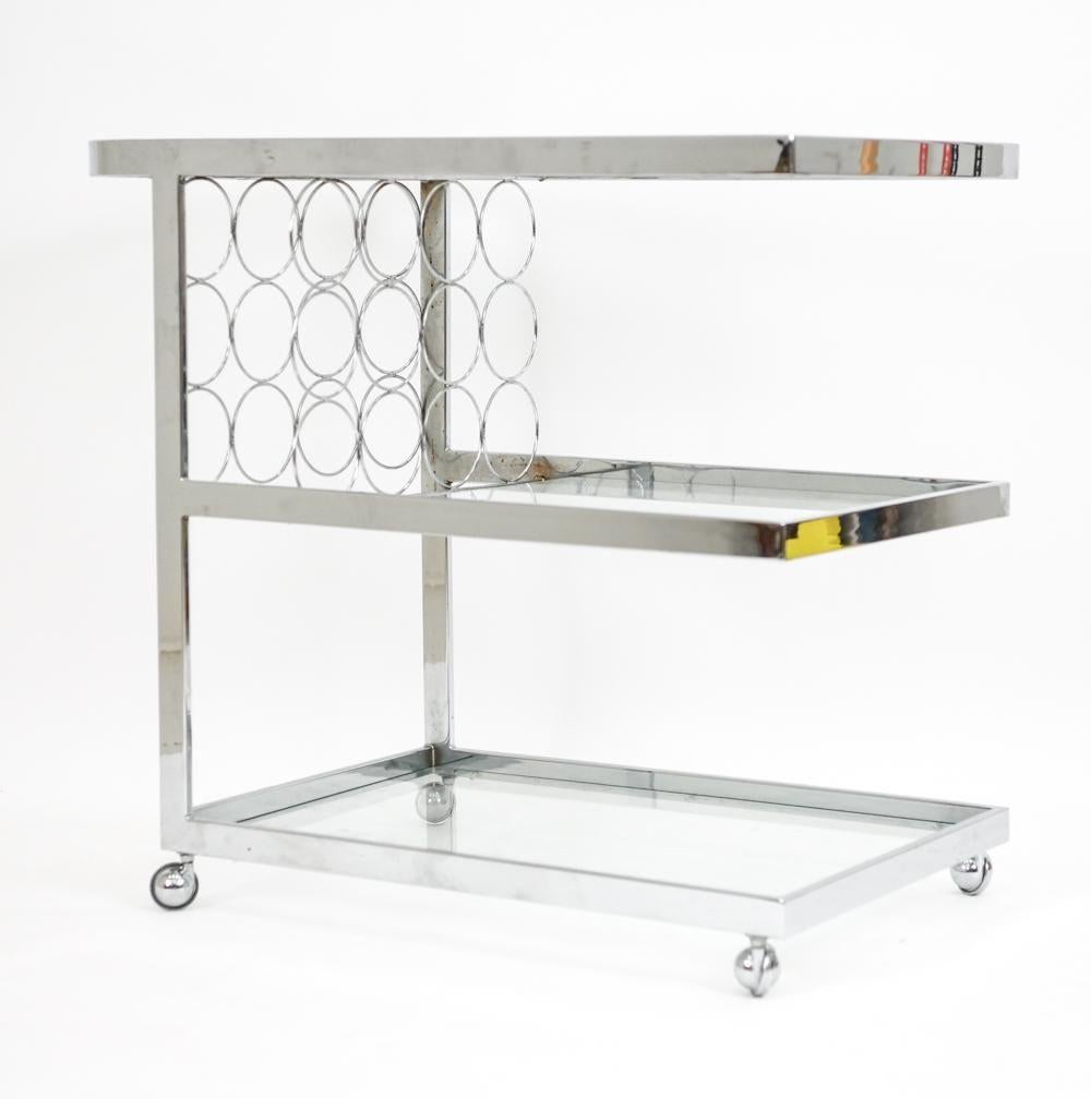 Chariot de bar ou de service chromé avec trois étagères en verre et des porte-bouteilles individuels.