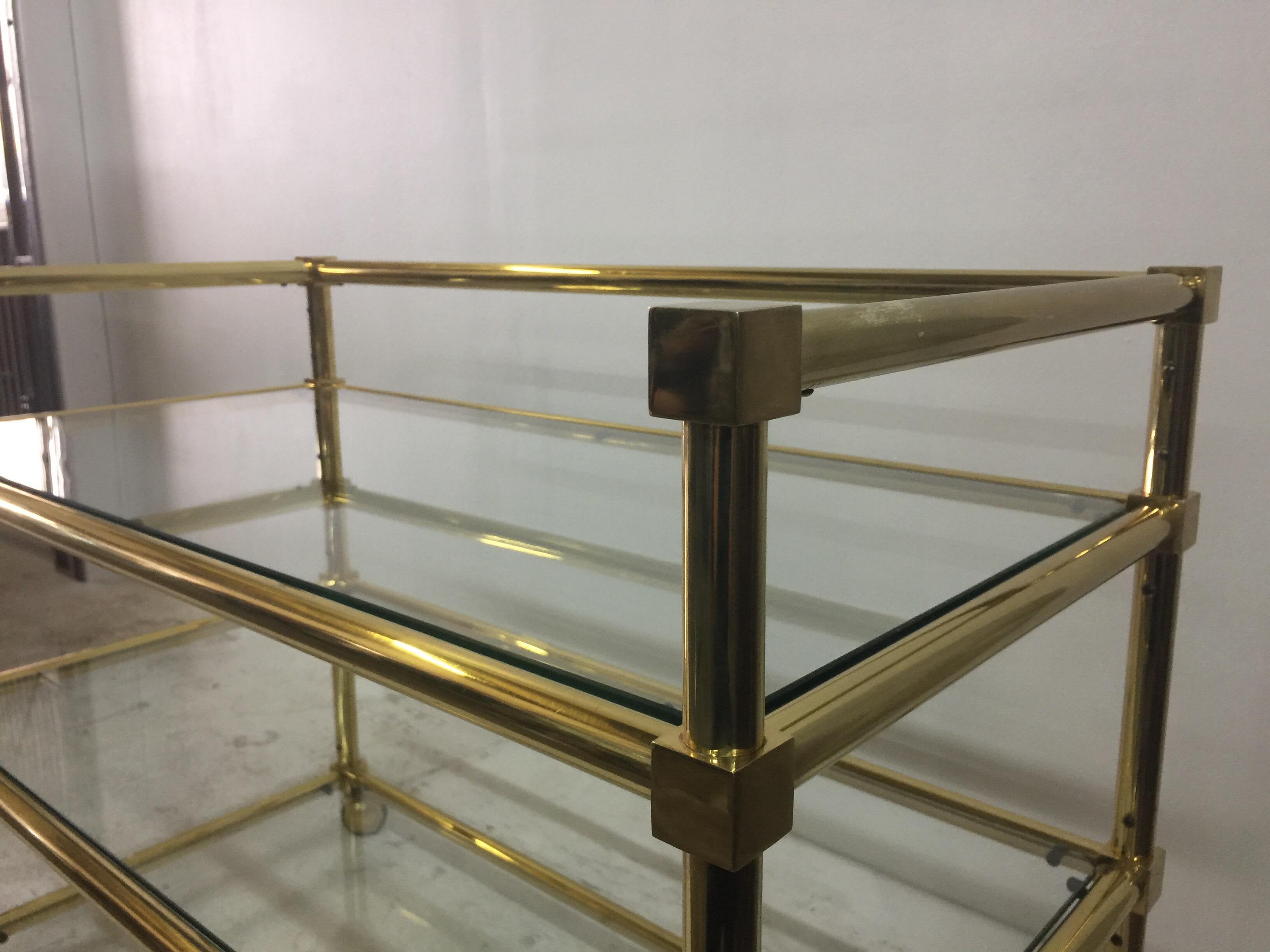 Attributed to Maison Jansen, this cart set on casters is perfectly proportioned and all vintage with heavily constructed tubular brass and square accent joints. Will play an important role in your bar décor needs. Three glass shelves and back