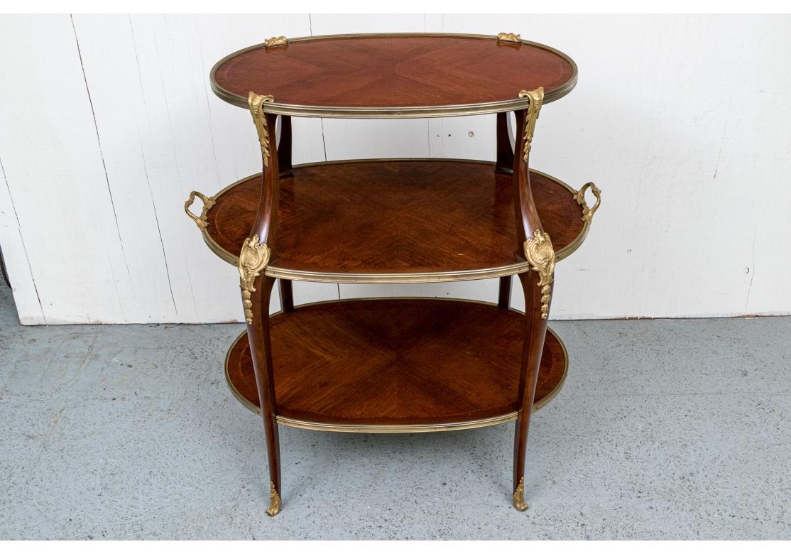 A French oval tiered stand with decorative Parquetry inlaid wood surfaces, a particularly decorative open form with Bronze lifting handles, trim and ornate leg caps.

Measures 34” wide by 19.5” deep by 38” high. 

Condition: Please see detail