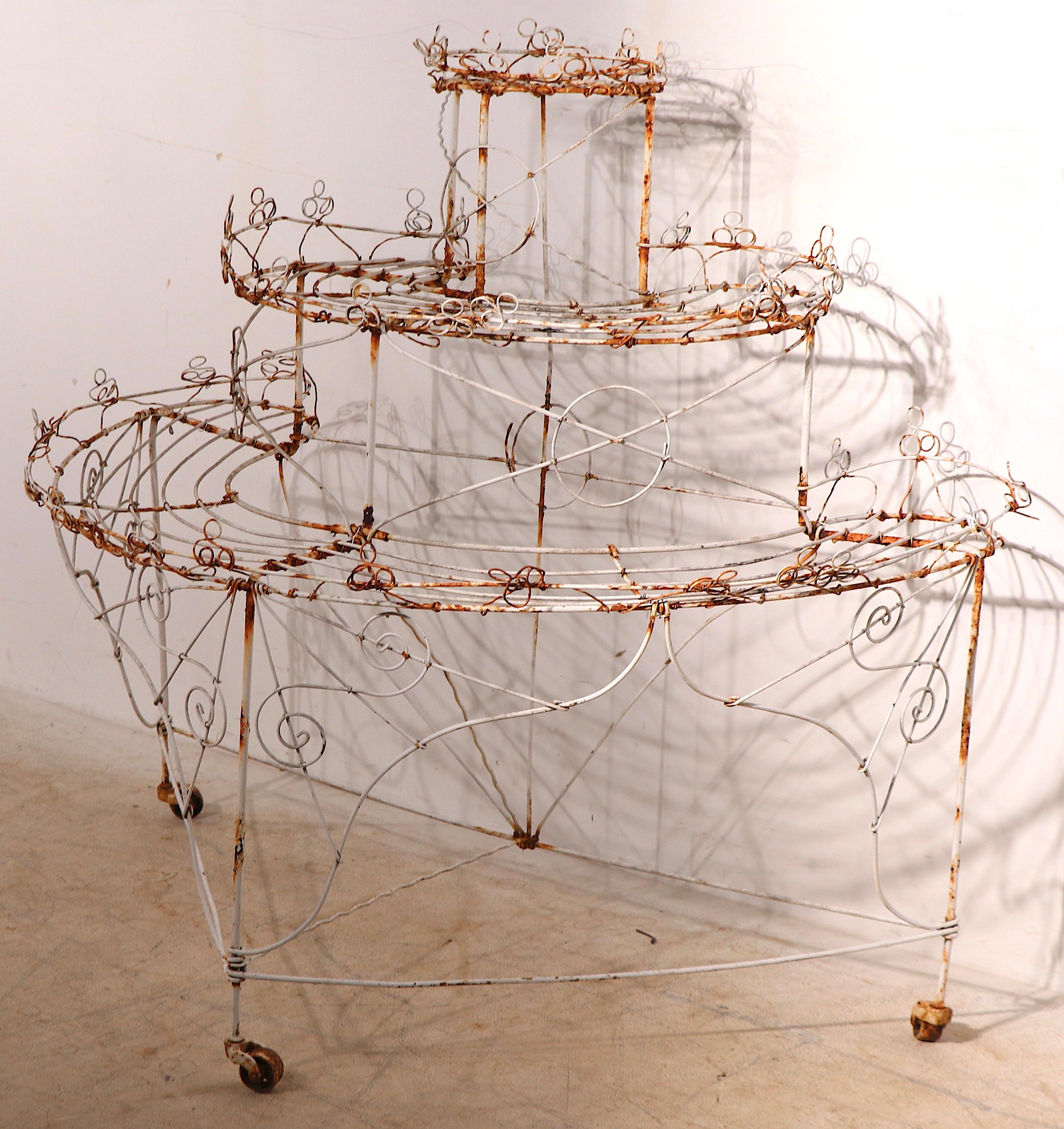 Charmant cache-pot en fil de fer à trois niveaux, de forme semi-circulaire, en finition d'origine vieillie. La pièce comprend trois étagères graduées, ( 38-30-20 in. H ) avec une garniture décorative en fil de fer à volutes. Original, état de