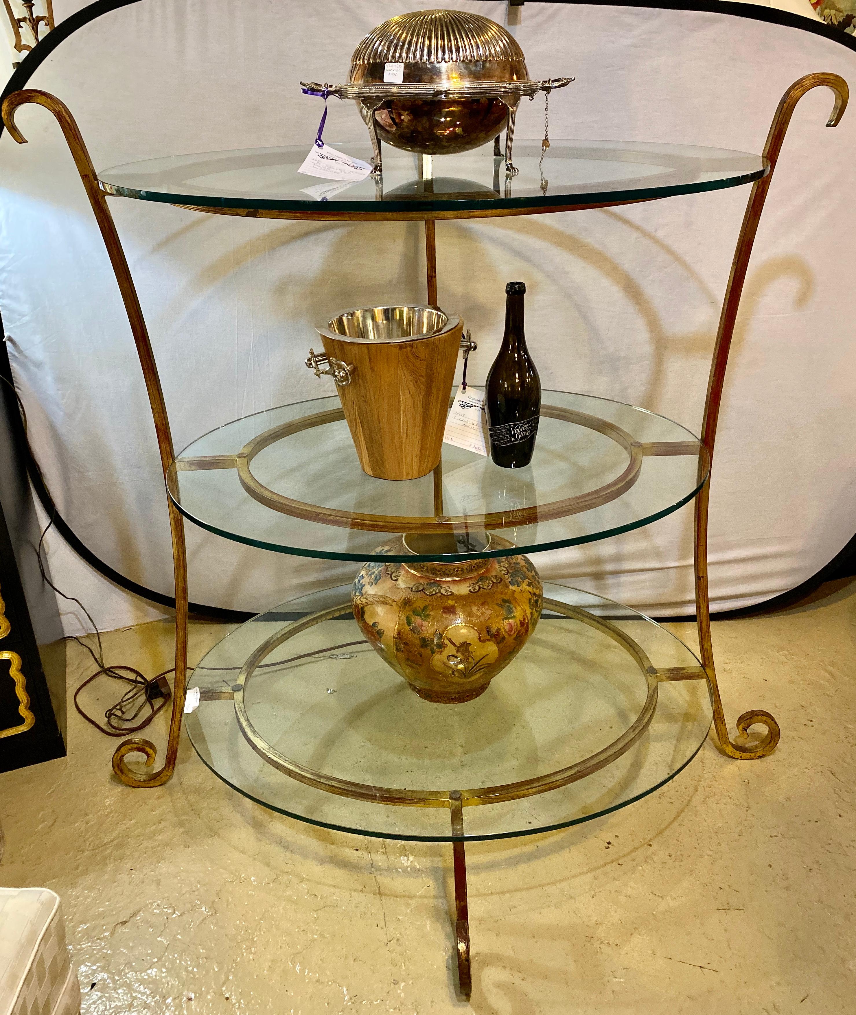 Three-tier glass and gilt metal étagère stand. Warm toned gilt metal curved legs that connect three circular bases that hold the glass. The wonderfully scrolled supports depict the Hollywood Regency era at its finest. This étagère can be used as