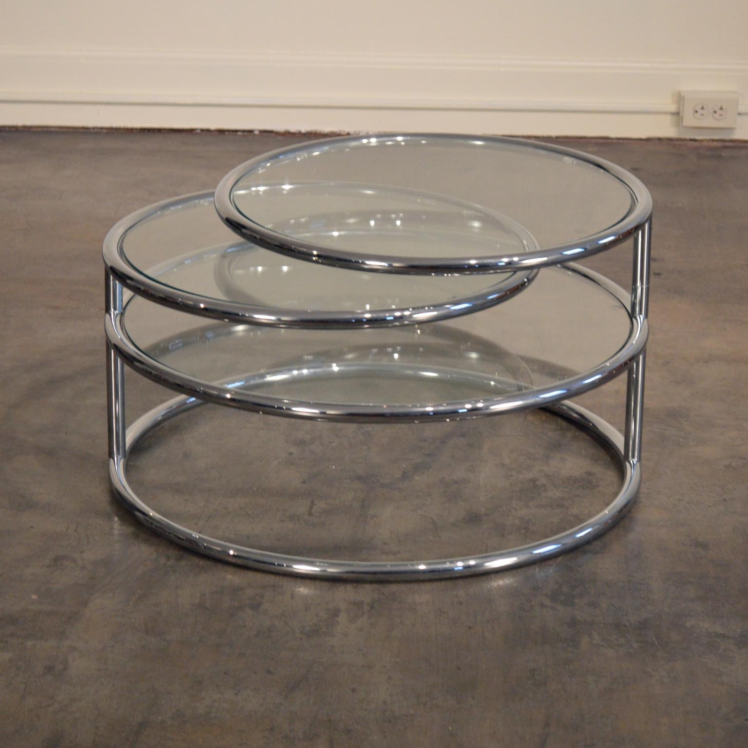Articulating three tier tubular chromed steel and glass cocktail table. Luxurious and expertly crafted, this modern classic is versatile and sturdy enough for entertaining and display. The two top shelves seamlessly swivel 360 degrees. The bottom