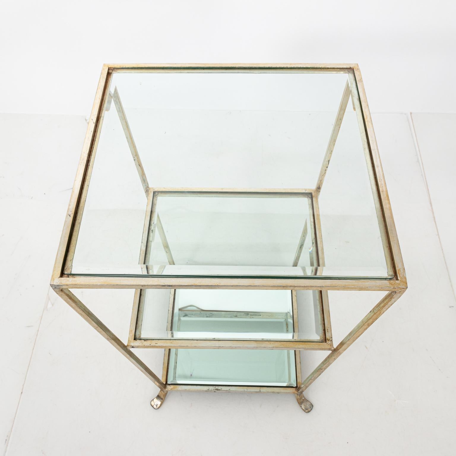 Three-tier metal side table with silver leaf, circa 1980s. The piece also features two beveled glass tops with a singular beveled mirror glass top on the lowest shelf. Please note of wear consistent with age including loss to silver leaf and heavy