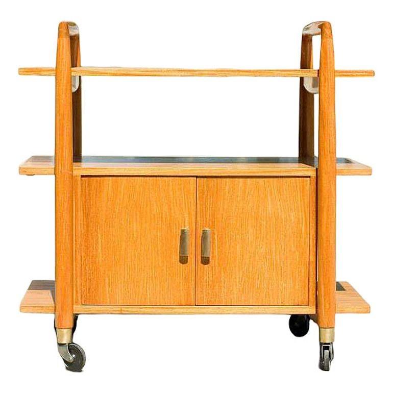 Blond three-tier Mid-century bar cart with an underneath storage cabinet. The cart features brass accents with four coaster wheels for easy travel from room to room. Reminiscent of the design styling made popular by the Heywood Wakefield