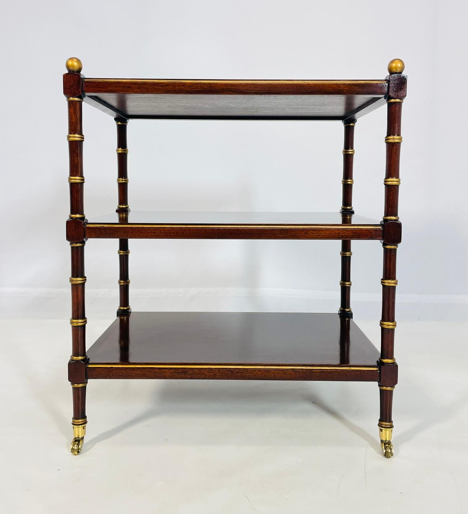Dieser exquisite dreistöckige Beistelltisch aus England aus den 1940er Jahren verleiht Ihrem Wohnbereich einen Hauch von Vintage-Charme. Gefertigt aus massivem Mahagoniholz  mit  Mit seinen verschlungenen, vergoldeten Akzenten, die ihm einen Hauch
