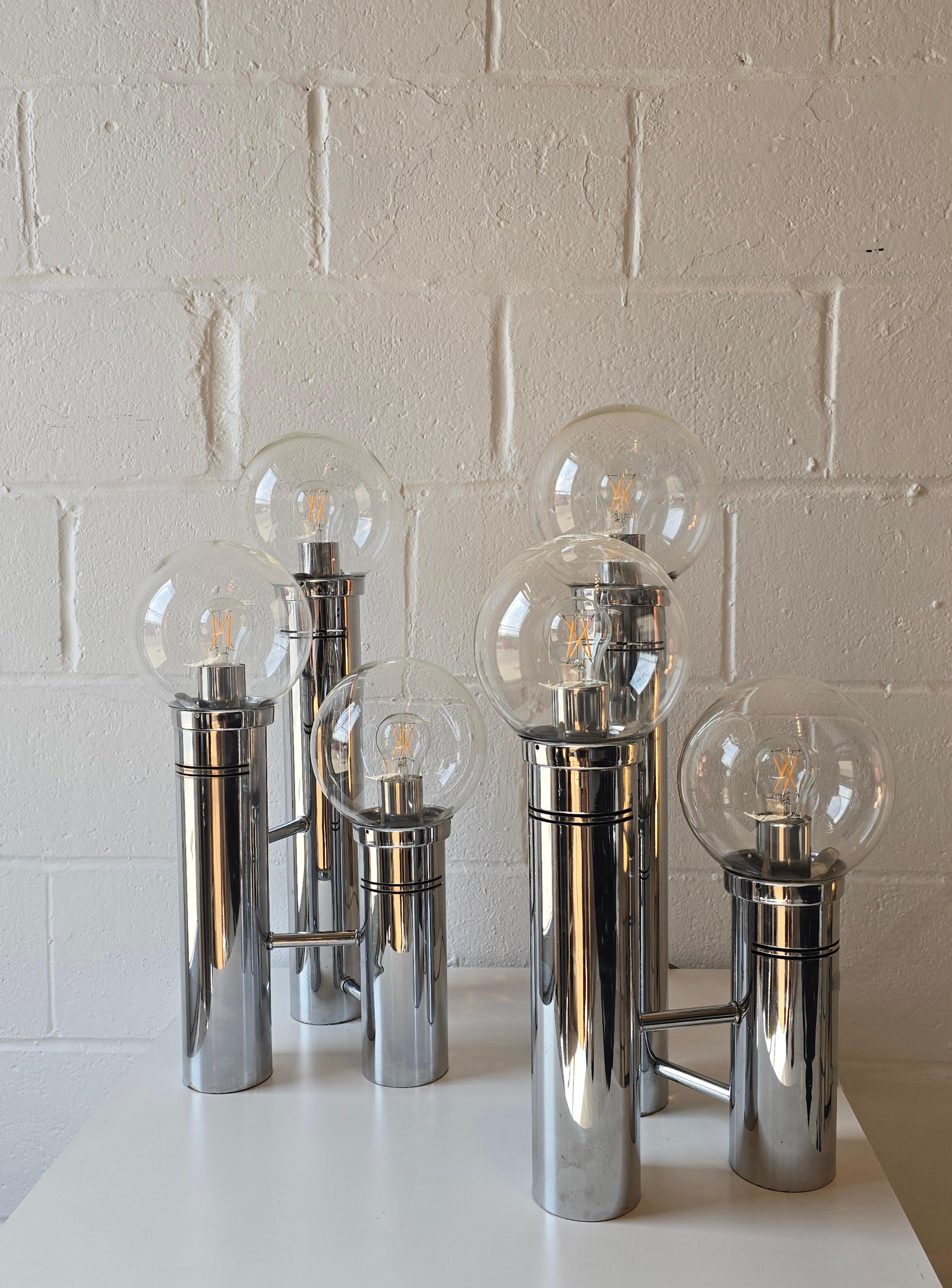 Splendide lampade da tavolo con globo di vetro e cromo. Questa graziosa lampada è composta da tre livelli cilindrici di diverse altezze, collegati alla base cromata con tre globi di vetro. I globi di vetro leggermente colorato coprono le lampadine.