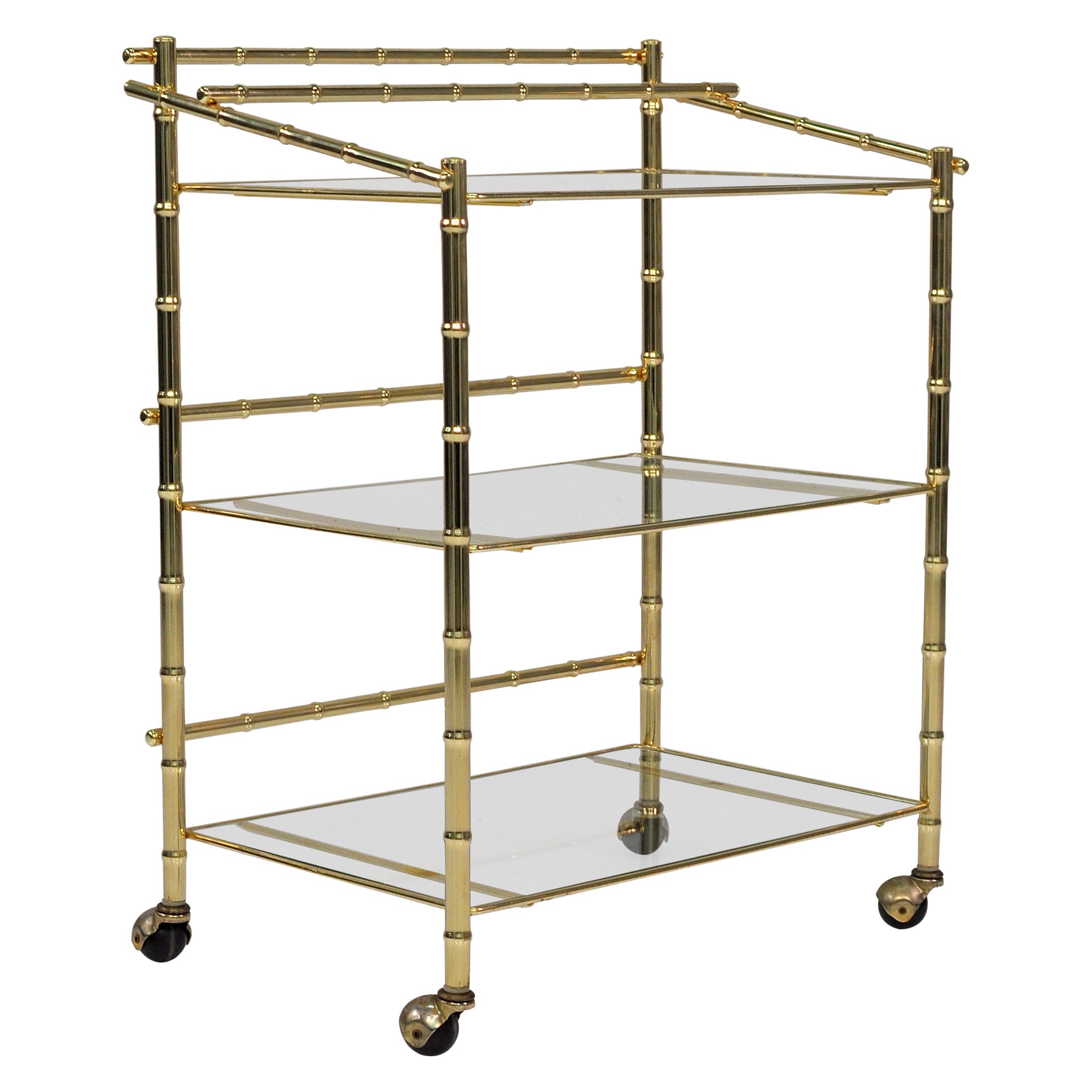 Carrito de bar rodante vintage Hollywood Regency de tres niveles de latón, imitación bambú y cristal, de los años 70. Elegante marco de imitación de bambú en latón pulido con tres estantes de cristal transparente. El nivel superior tiene una barra