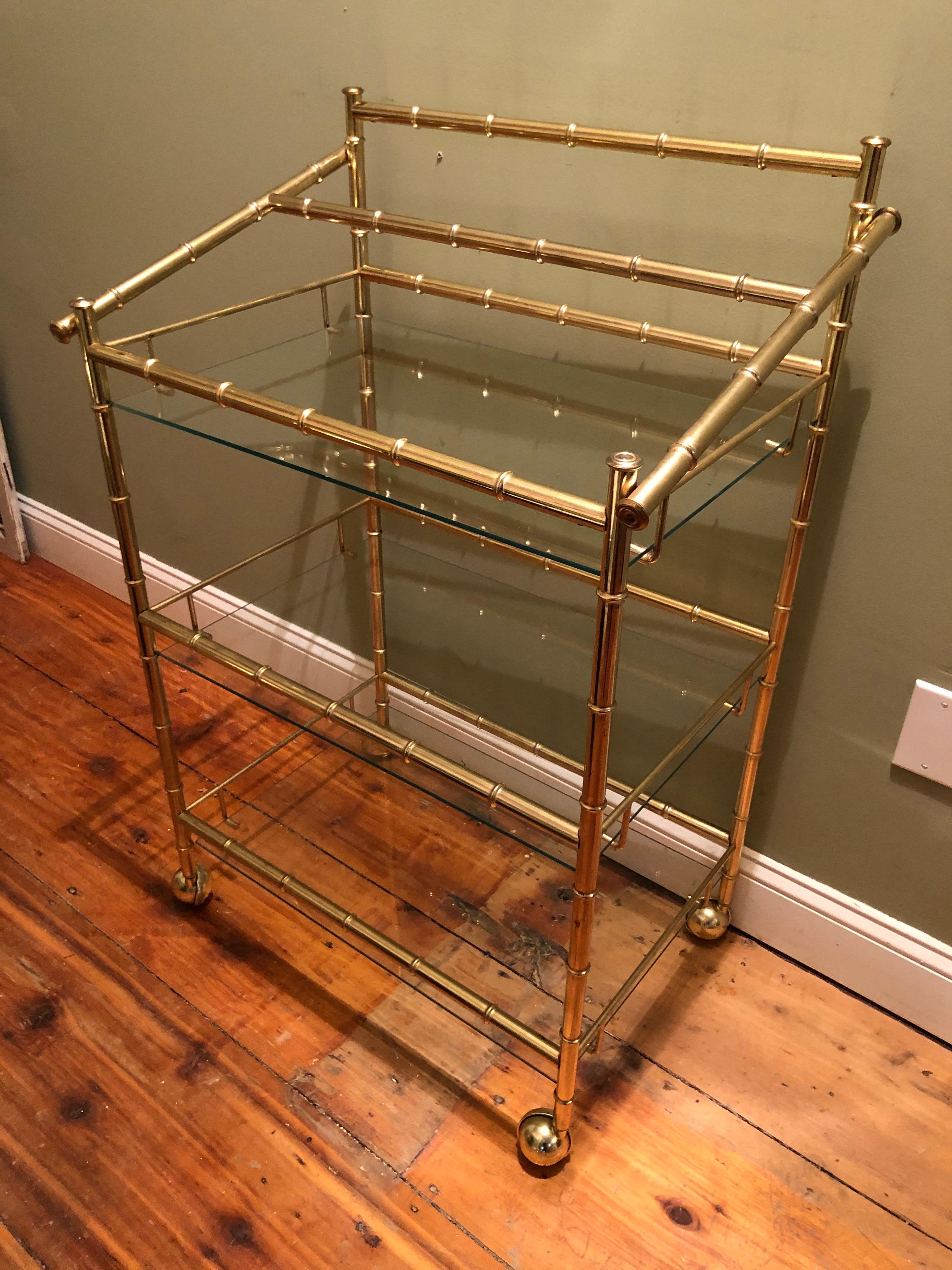 Three-tiered brass bamboo bar cart. The perfect entertaining piece. Lightweight and easy to move around. Brass bamboo accent frame with clear glass shelves. Top tier has a place to hold bottles. Nice large round brass castors. There is a twelve inch