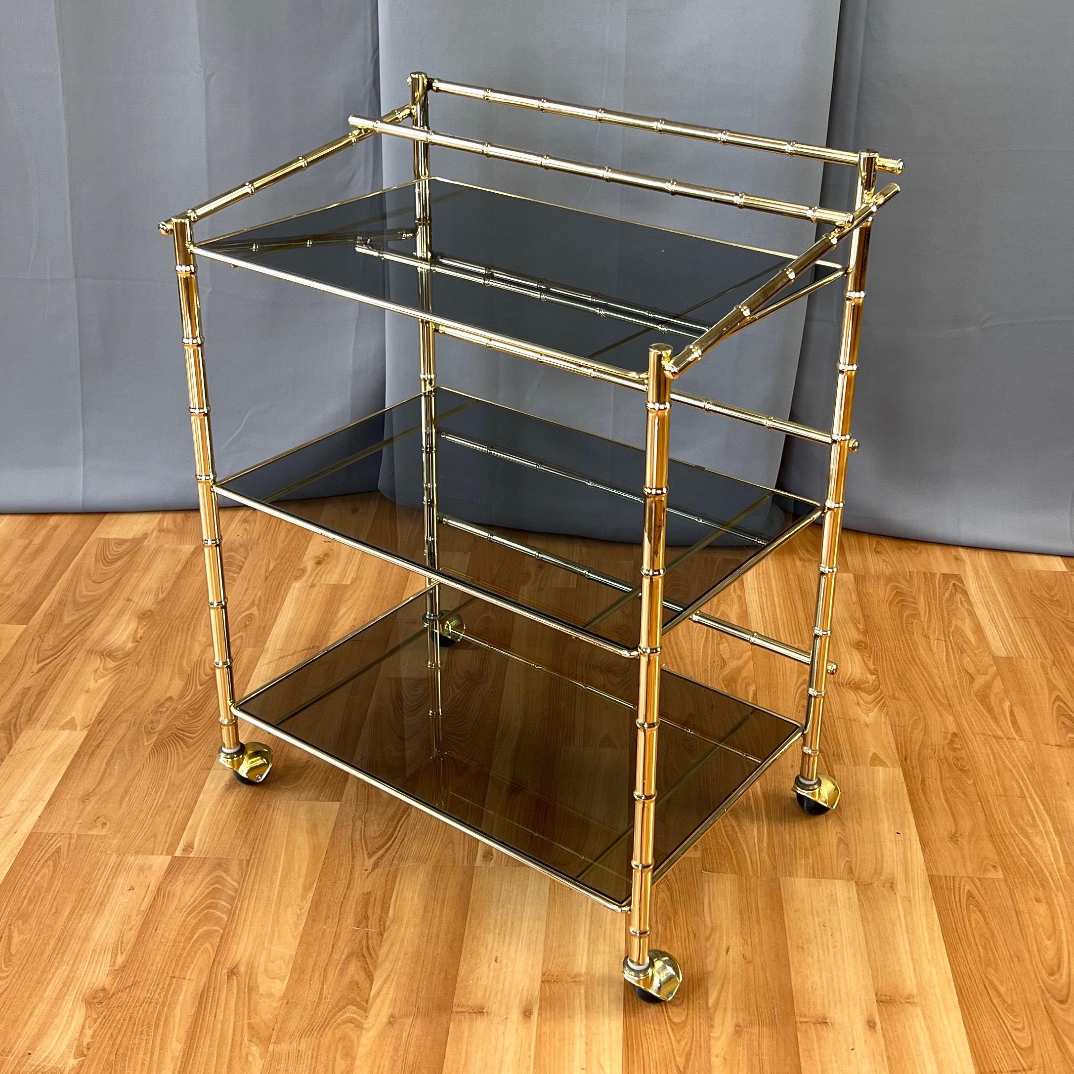 A 1970s Hollywood Regency brass faux bamboo bar cart or serving cart with three dark smoked glass tiers.

Very classy design defined by clean lines and just the right amount of Chippendale-like bamboo-accented style. Three tiers with spacious,