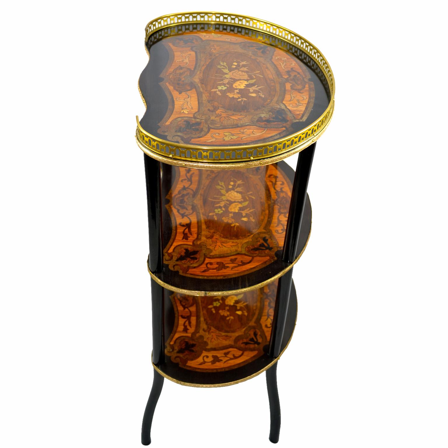 A beautifully inlaid three-tier kidney shaped desert table, each tier has an ebonized border, the four shaped legs are also ebonized. Each tier is inlaid with the same pattern of exotic woods with a central cartouche of roses. The top has a gilded